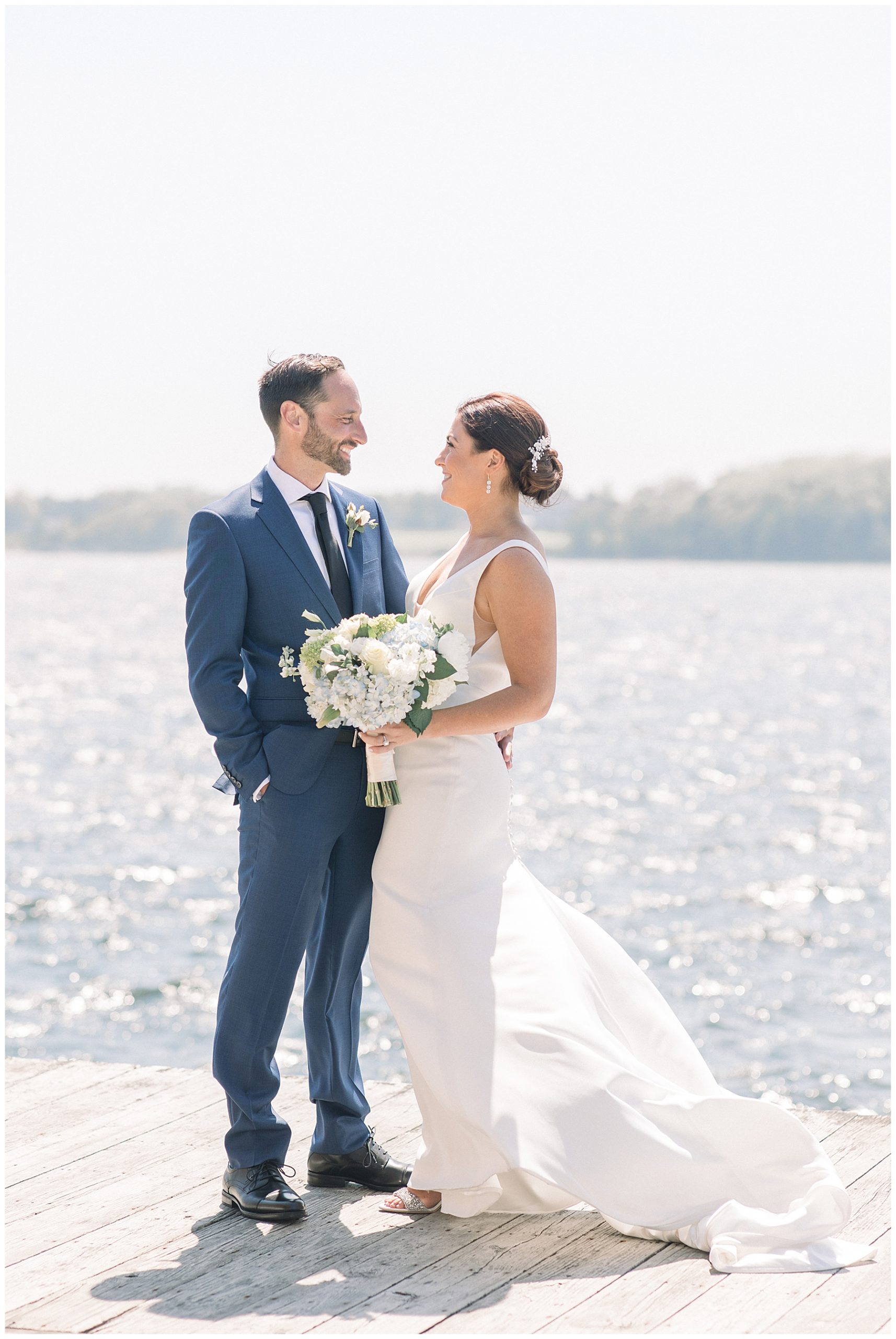 Bride + Groom stand on deck by the water at Bristol Harbor RI