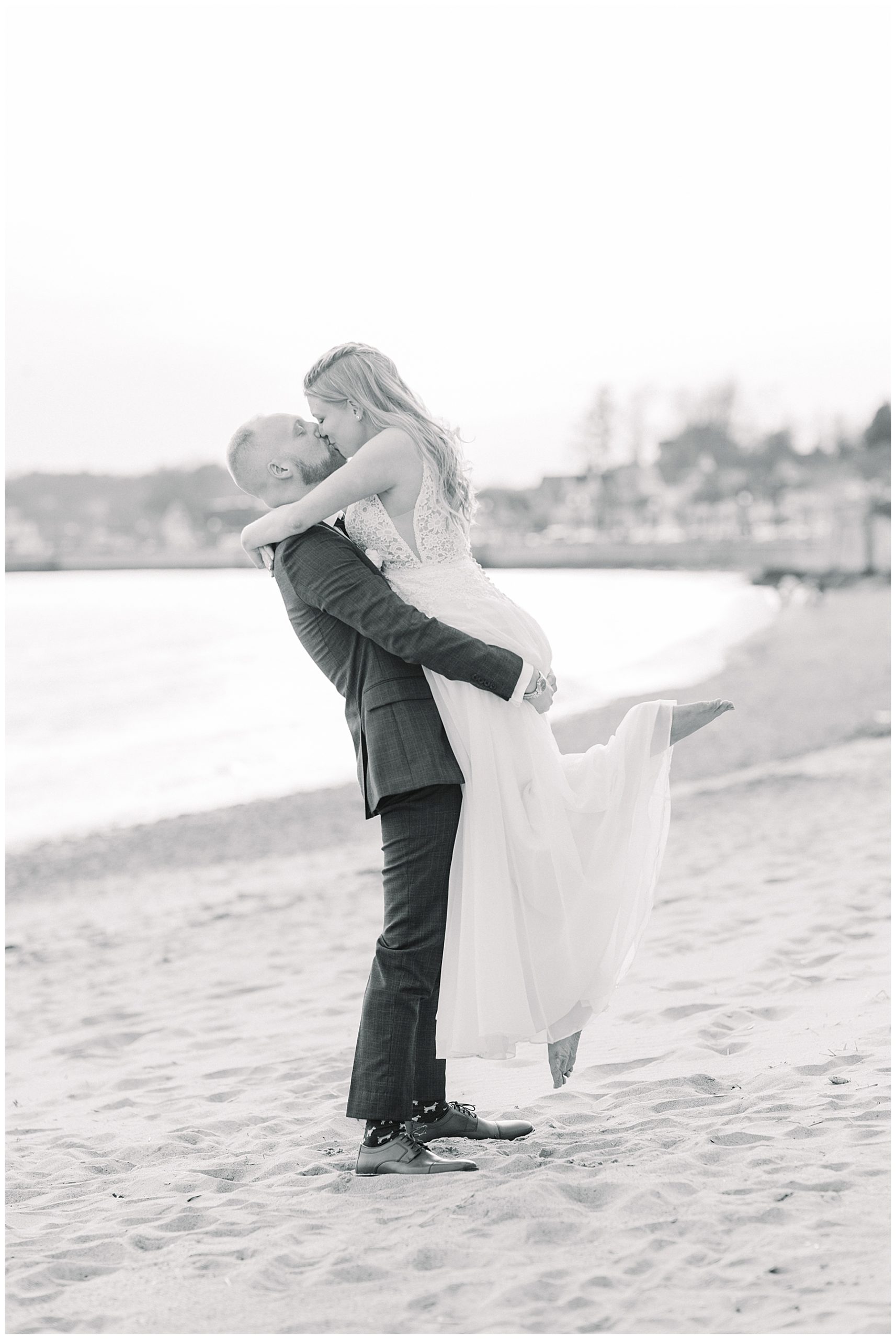 husband lifts wife up during beach wedding photos