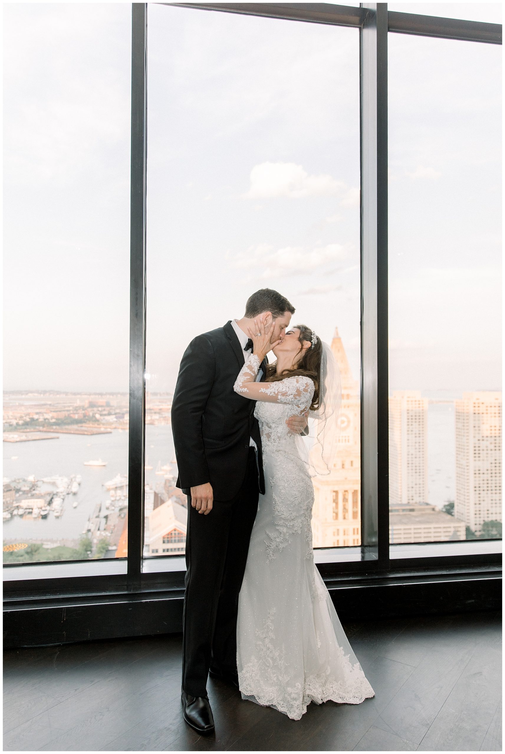 newlyweds kiss at the State Room: A Longwood Venue with the Boston skyline behind them