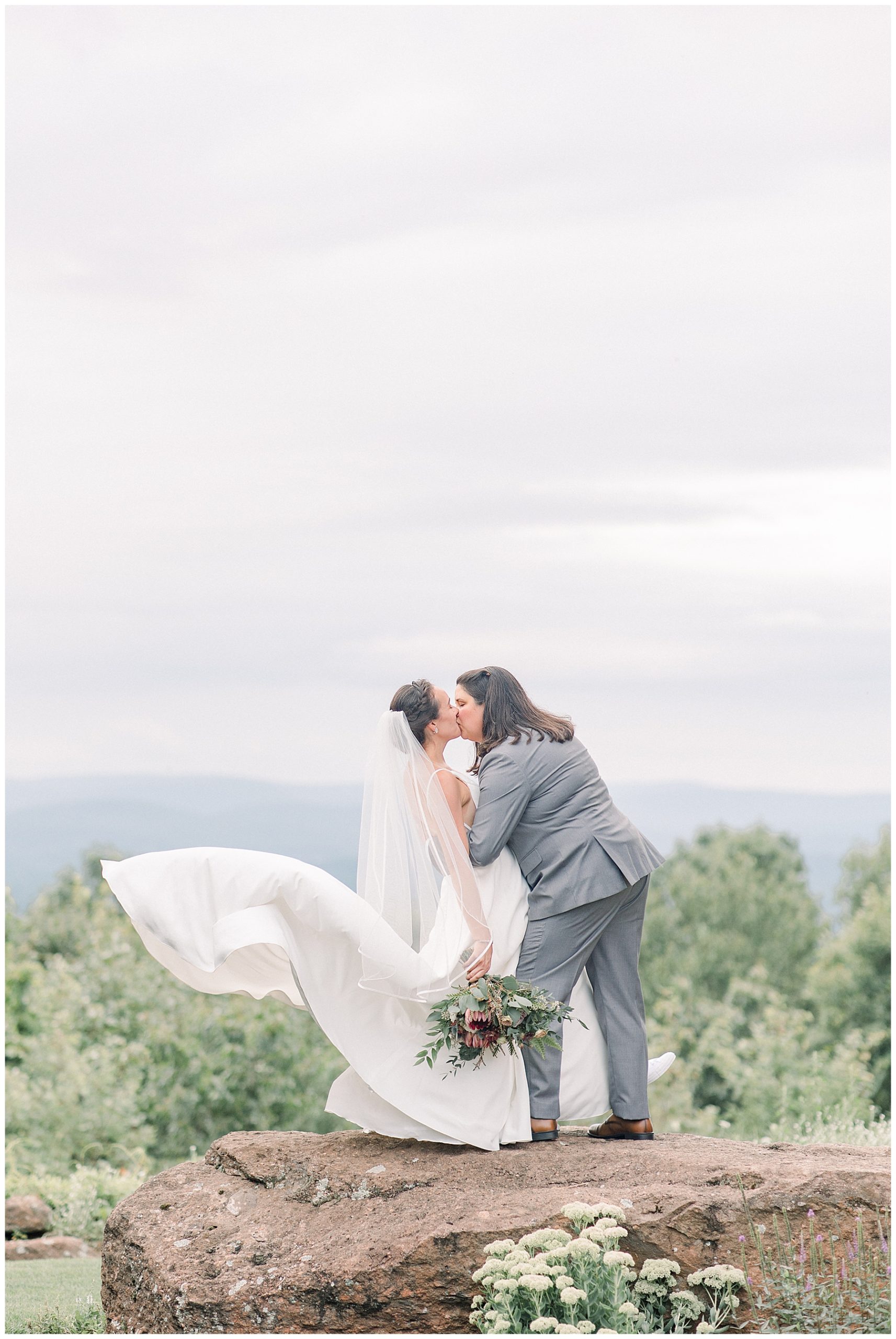 newlyweds kiss on rock overlooking mountainside