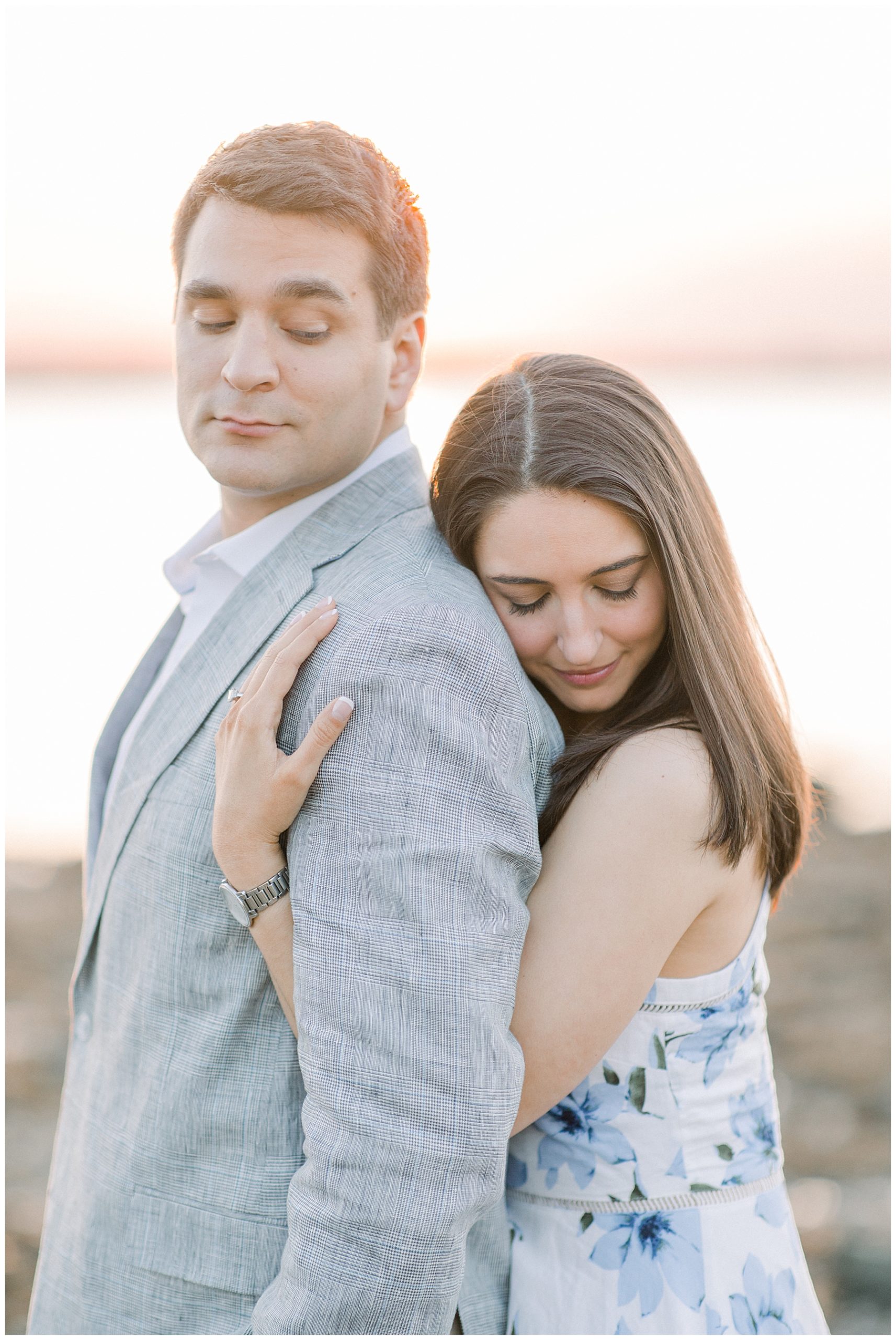 woman hugs her fiance from behind as they look down 