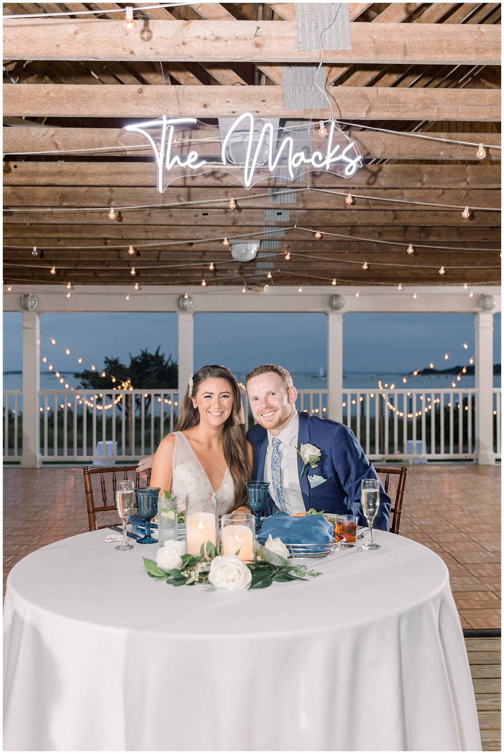 bride and groom sit at their table with custom light above them at Shining Tides Wedding