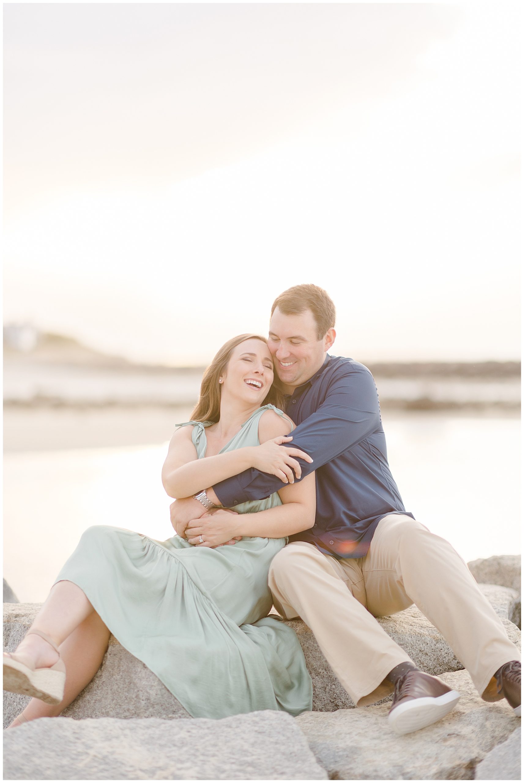 candid moment of couple sitting and laughing on a rocky shoreline 