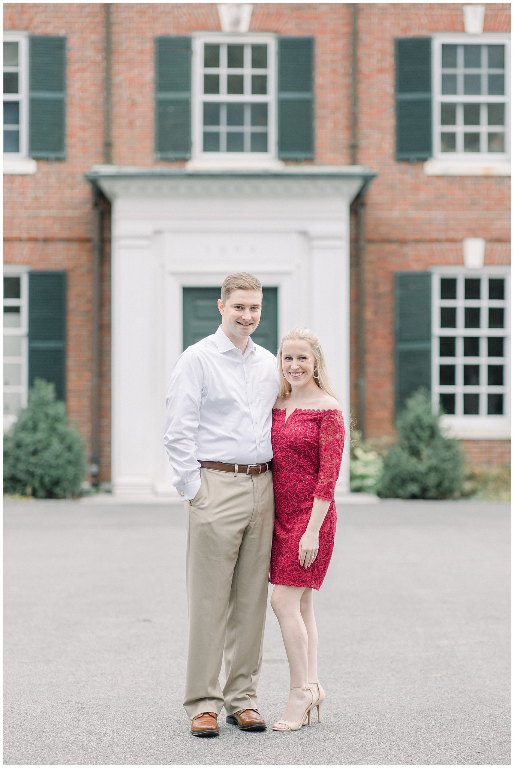 woman in red dress stands with her fiance in front of the Bradley Estate