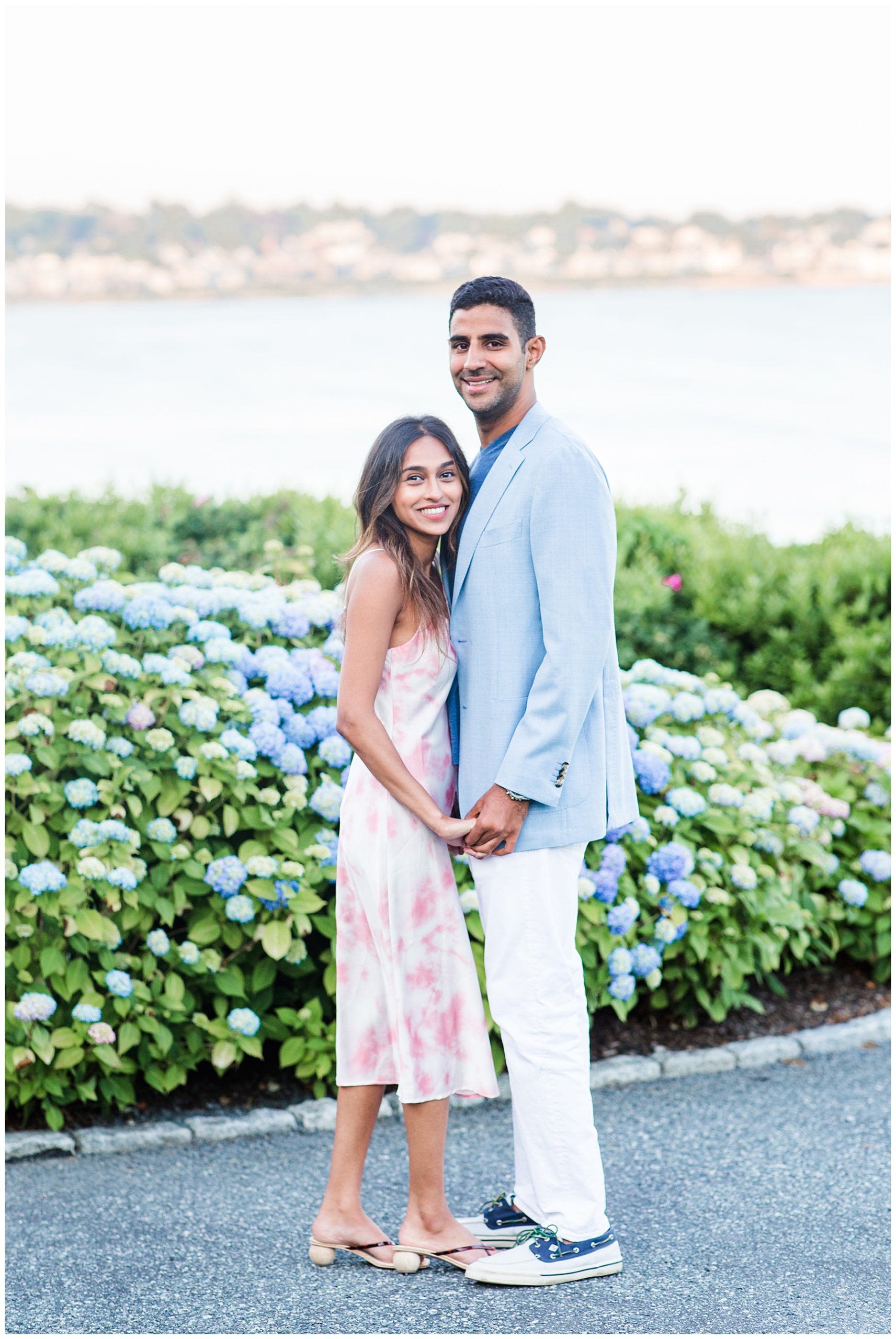 couple stand in front of beautiful blue flowers overlooking the ocean