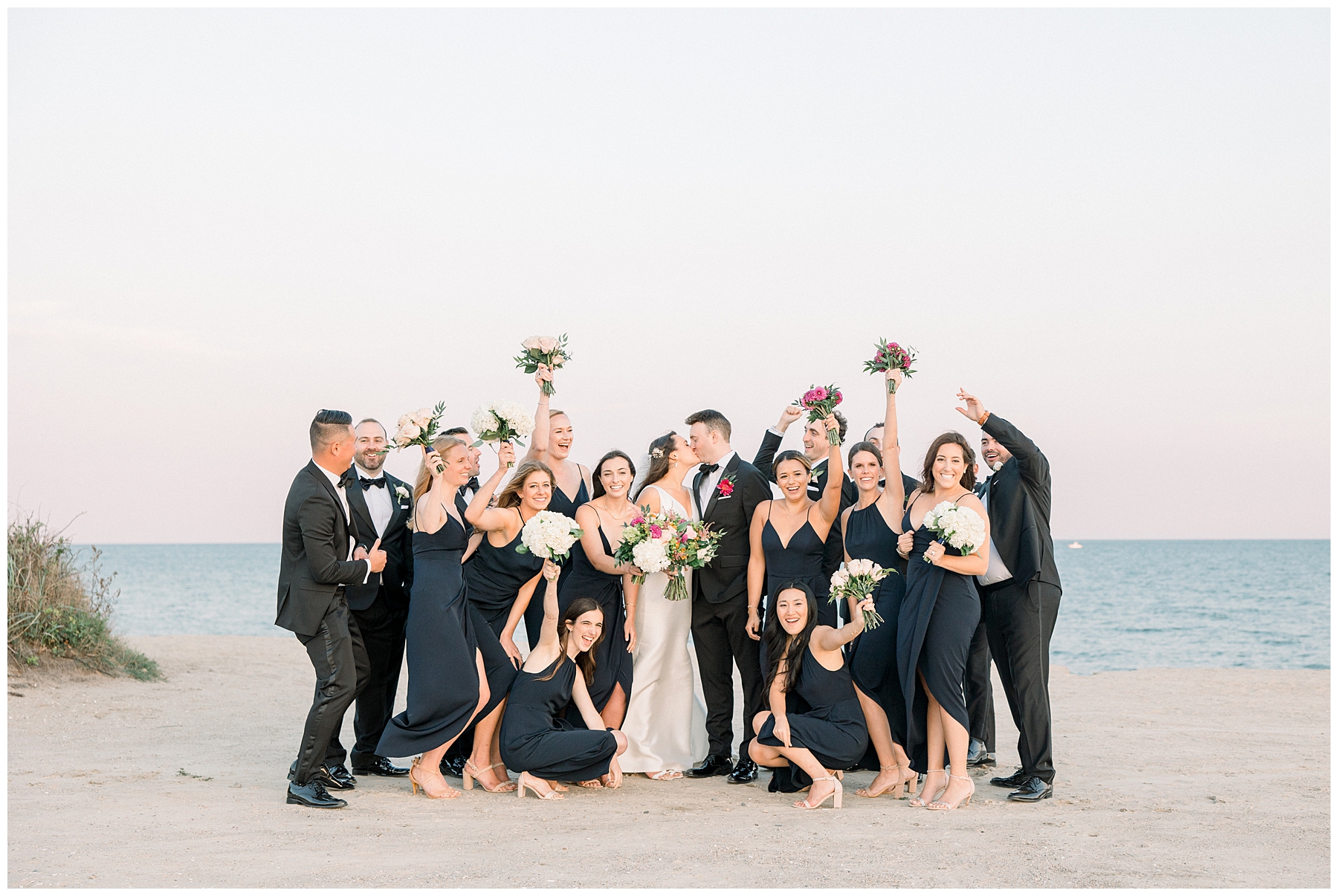 Bridal party gathers around bride nad groom on Cape cod beach