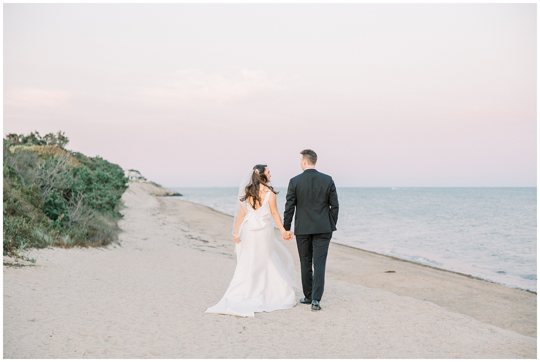 newlyweds hold hands and walk down the beach 