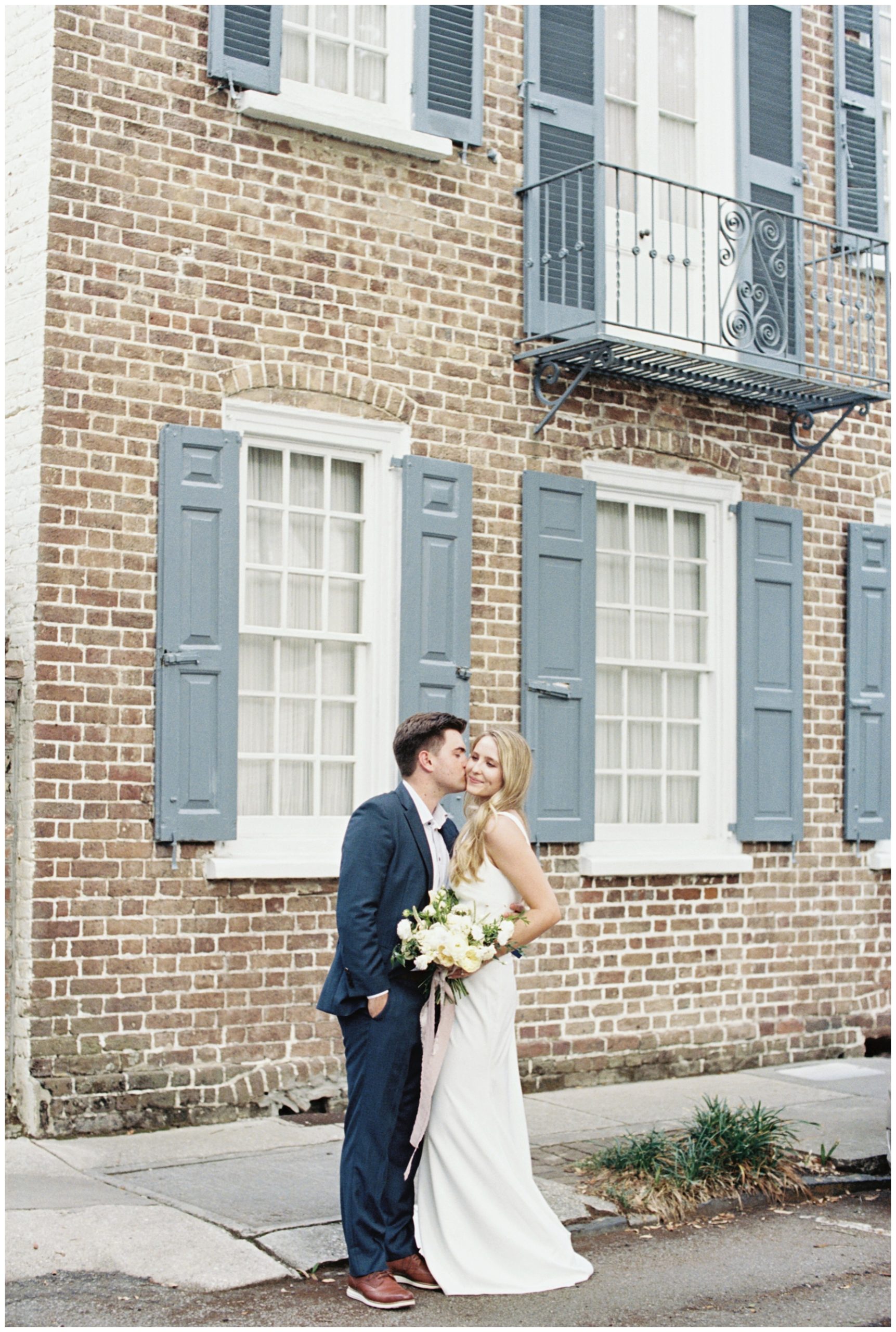 newlyweds in front of brick house with blue shutters in downtown Charleston SC