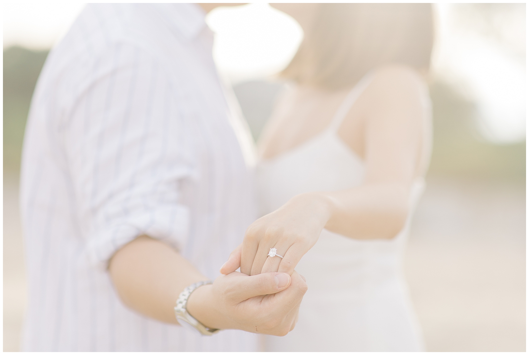 couple hold out their hands intertwined to show engagement ring 