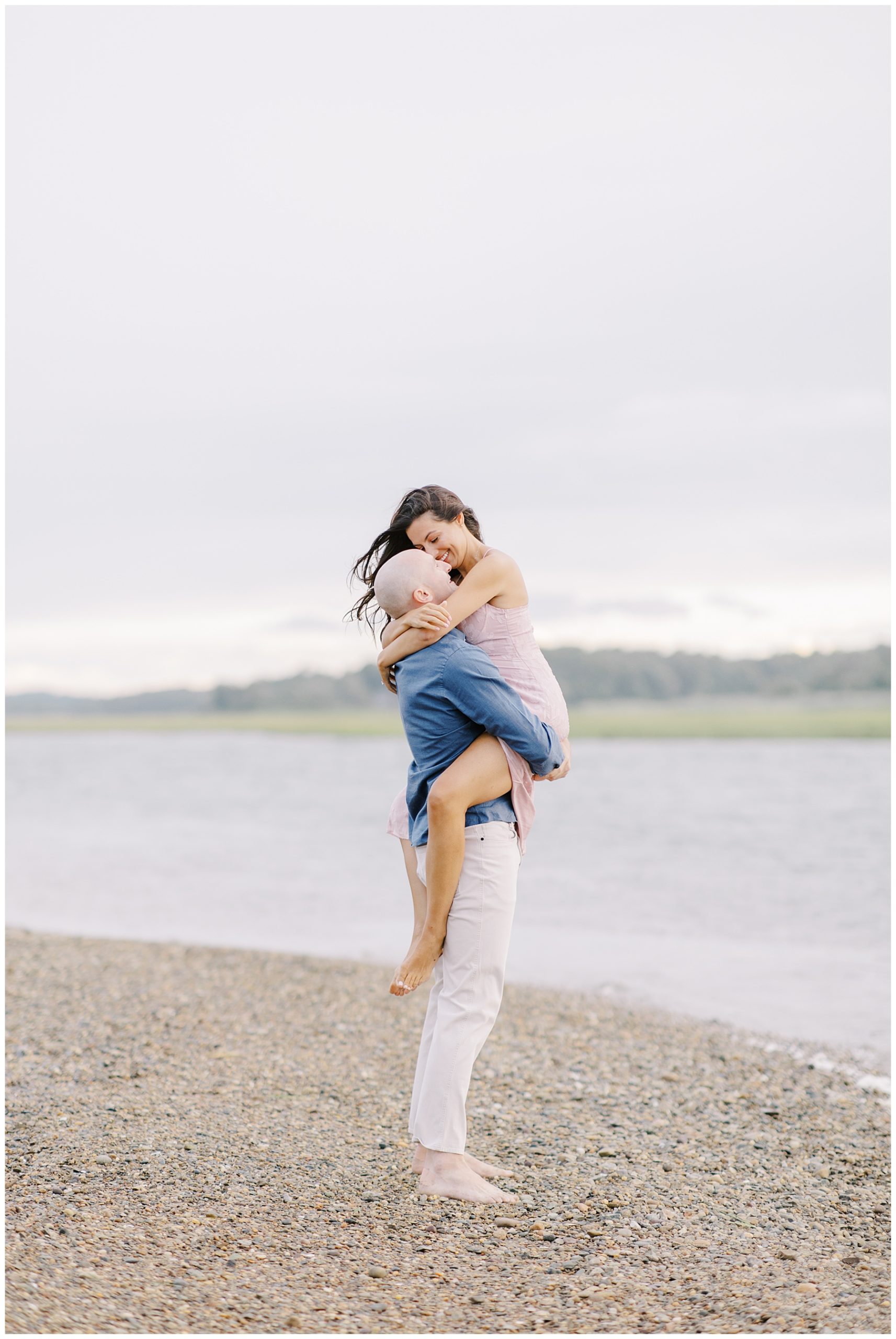 guy holds his fiance in his arms standing on the beach 