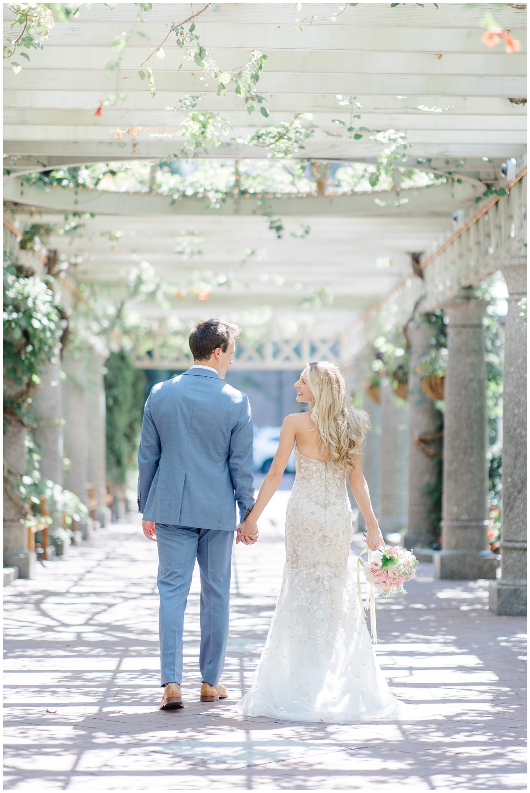 couple hold hands as they walk under pergola 