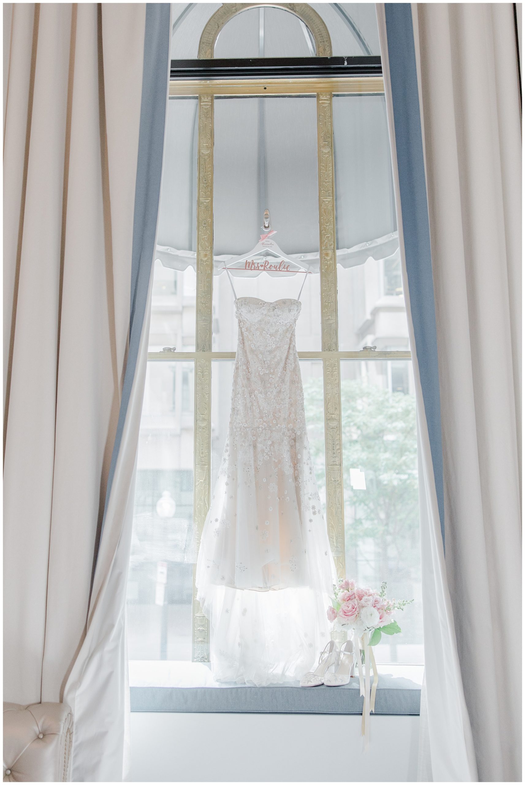wedding dress hangs in front of large window 