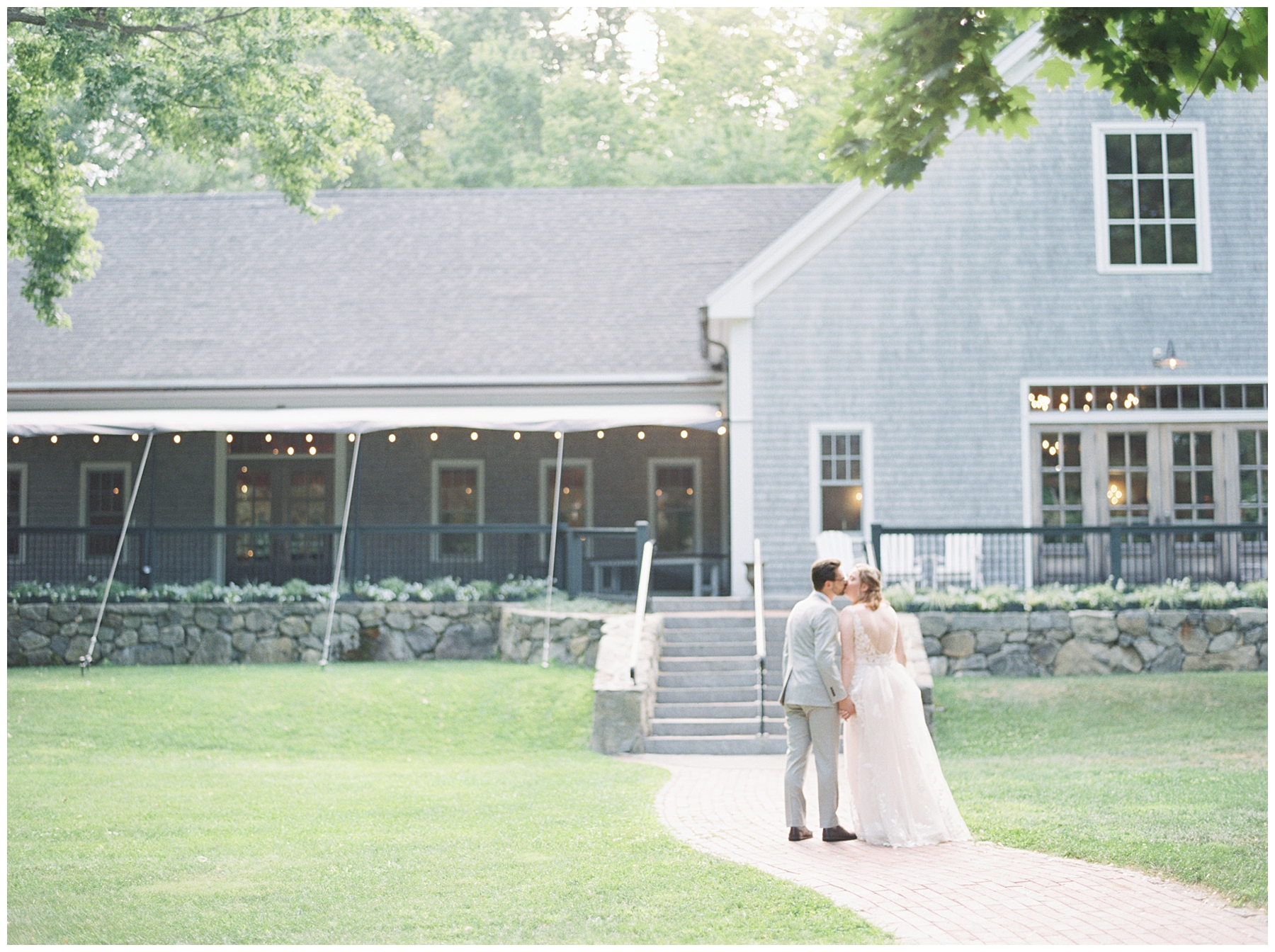 couple kiss in front of Thompson Inn and Cyderhouse Wedding venue in New Hampshire 
