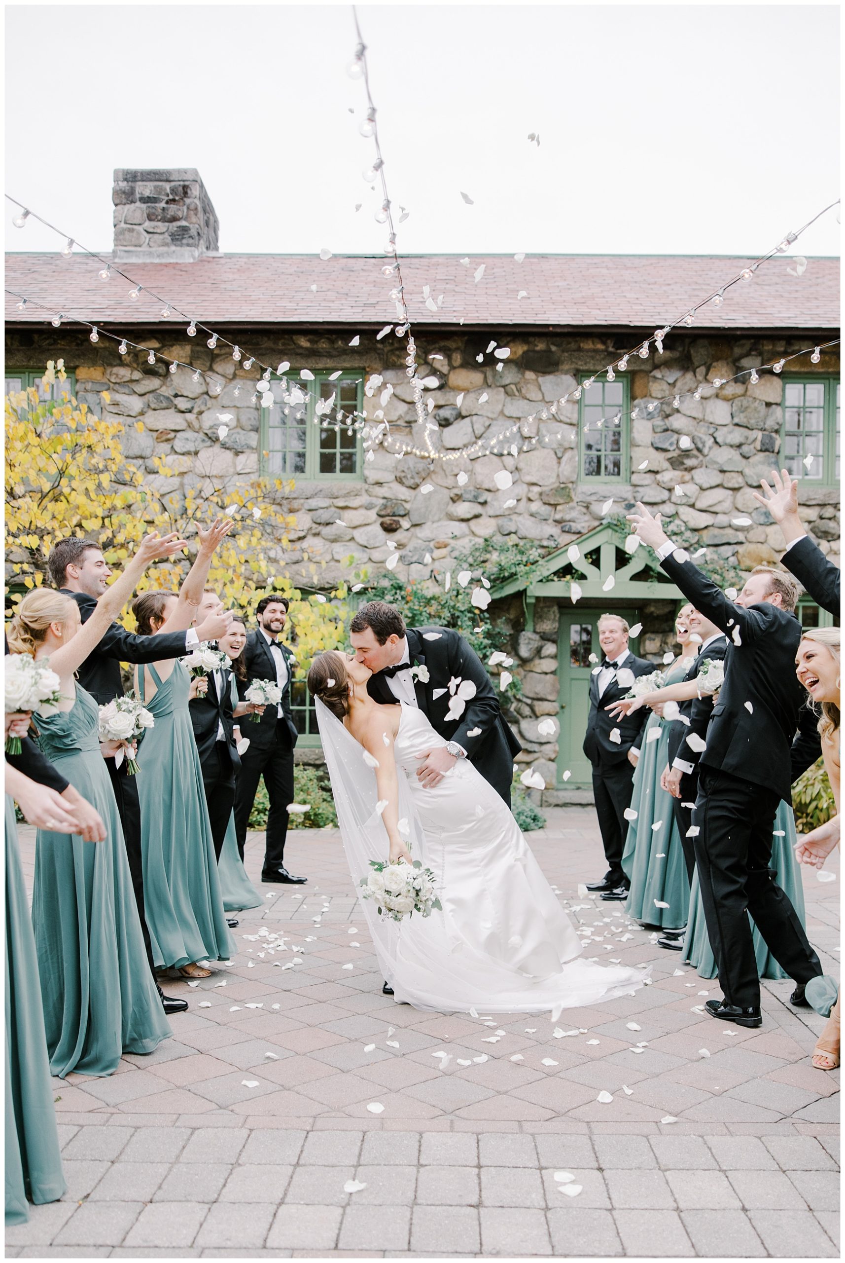 wedding party tosses white petals around couple kissing