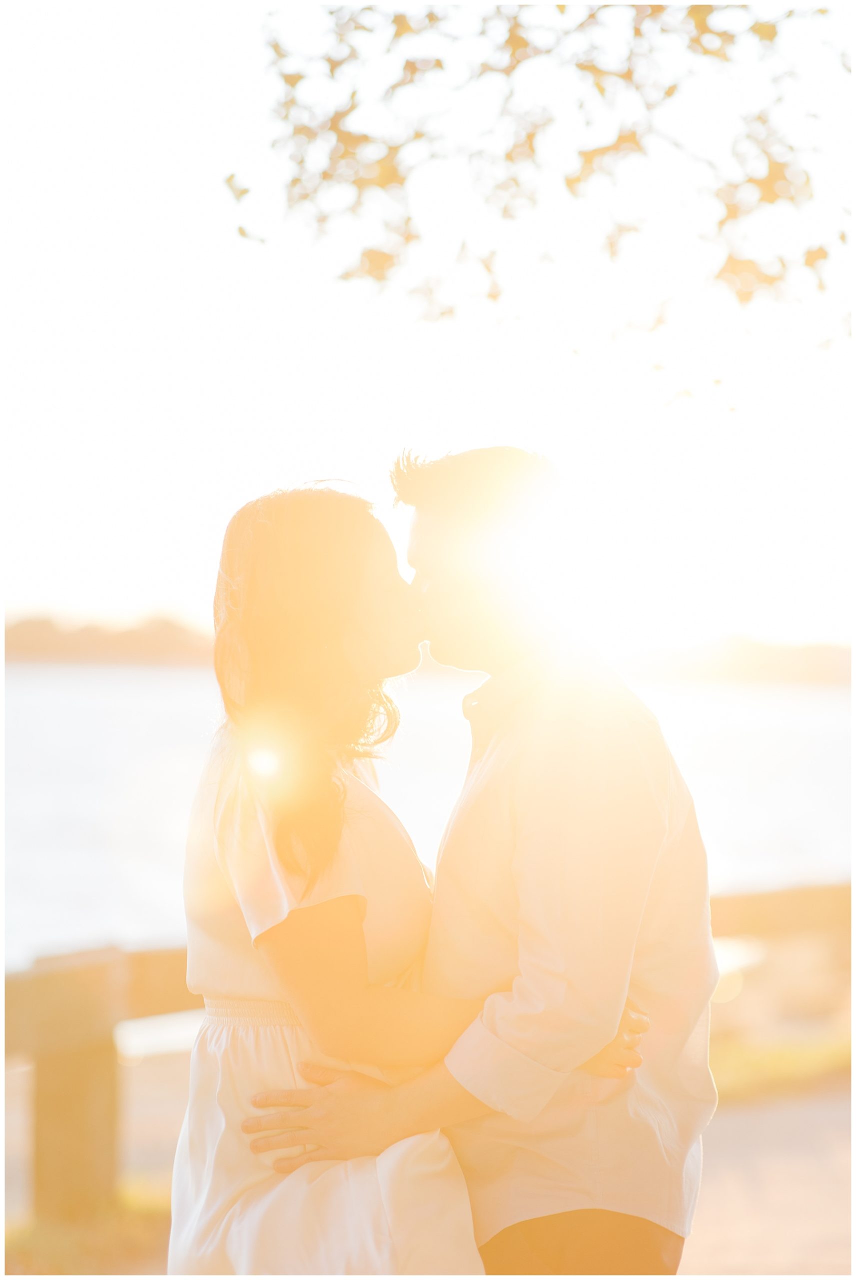couple kiss by the water as the sun sets behind them