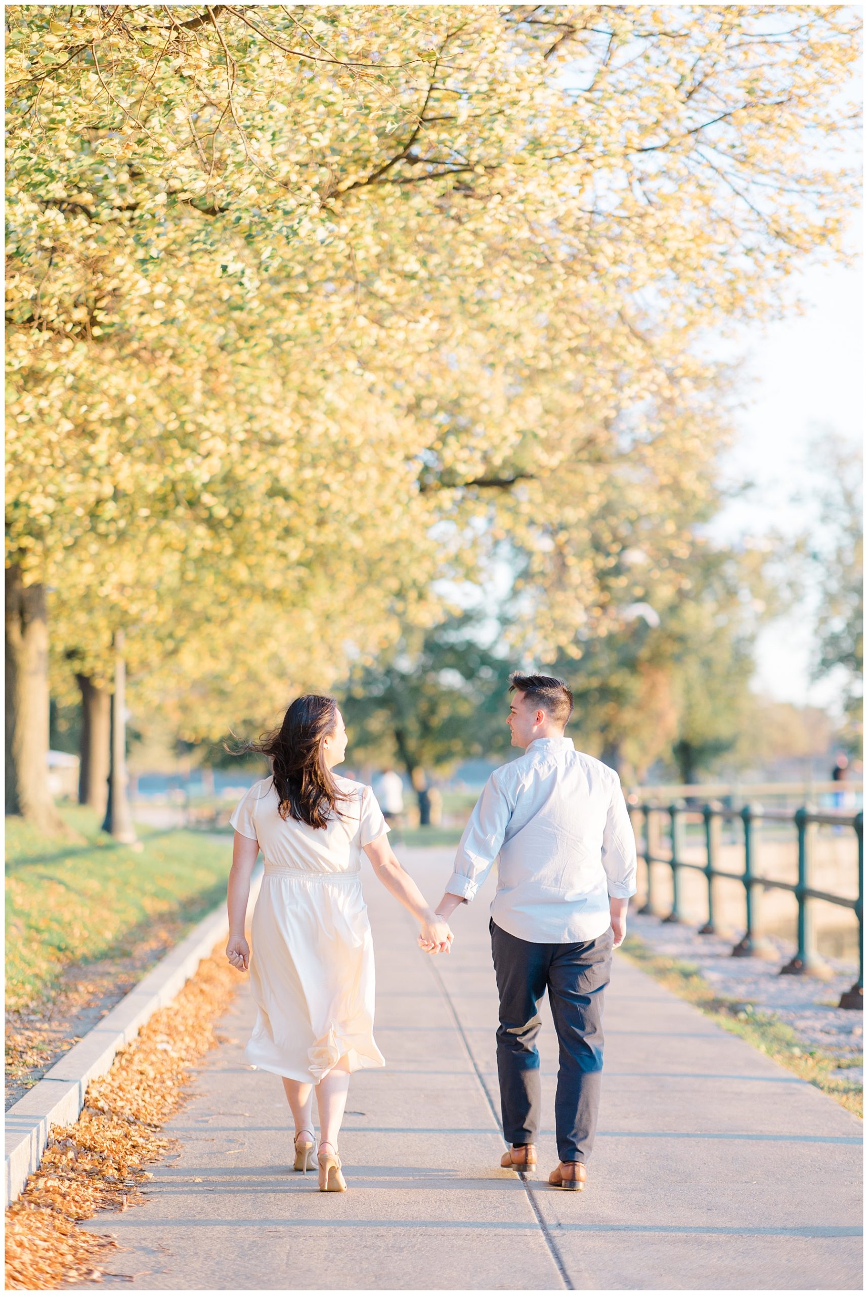 couple walk together holding hands with fall trees surrounding the sidewalk 