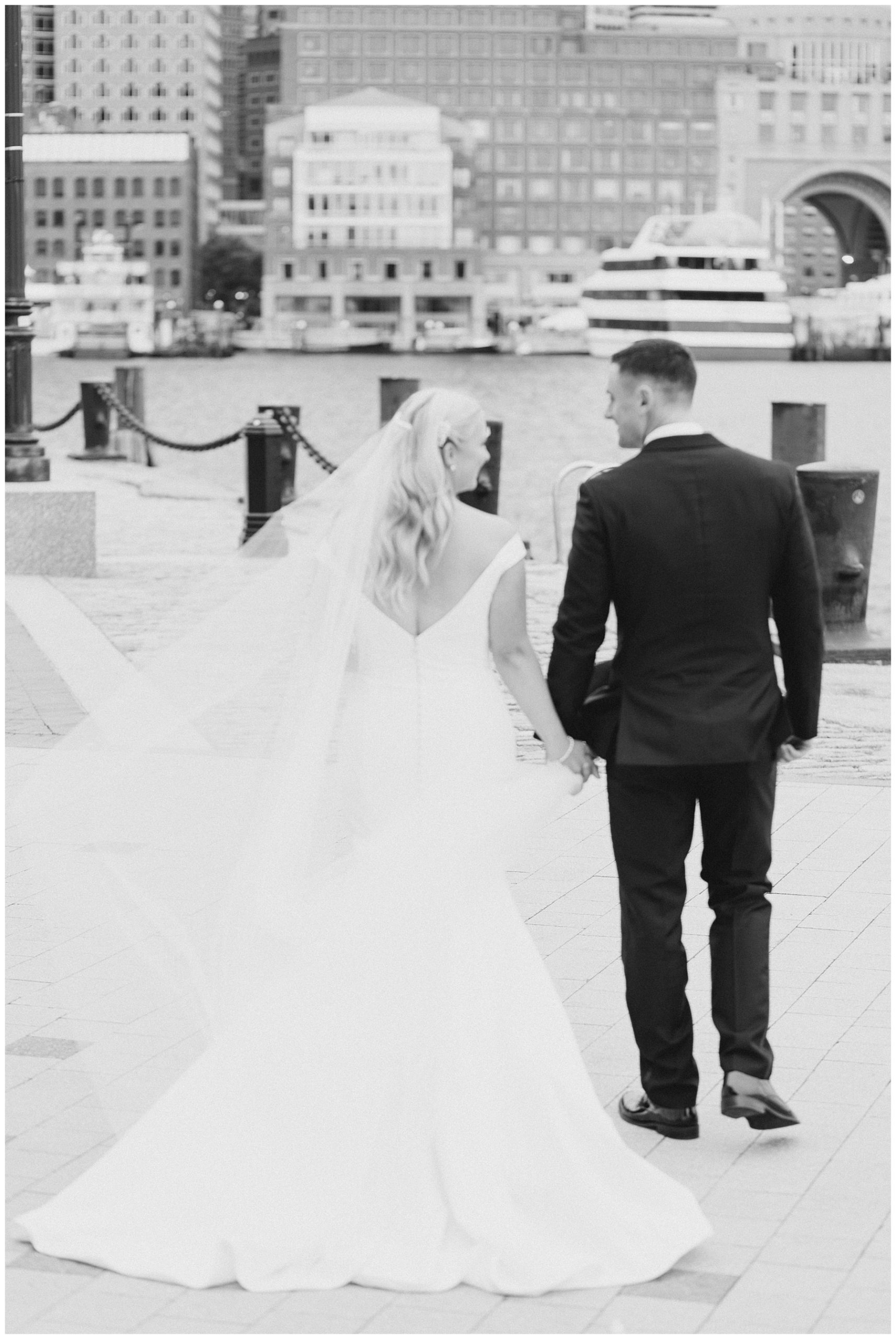 newlyweds holding hands facing harbor in downtown Boston