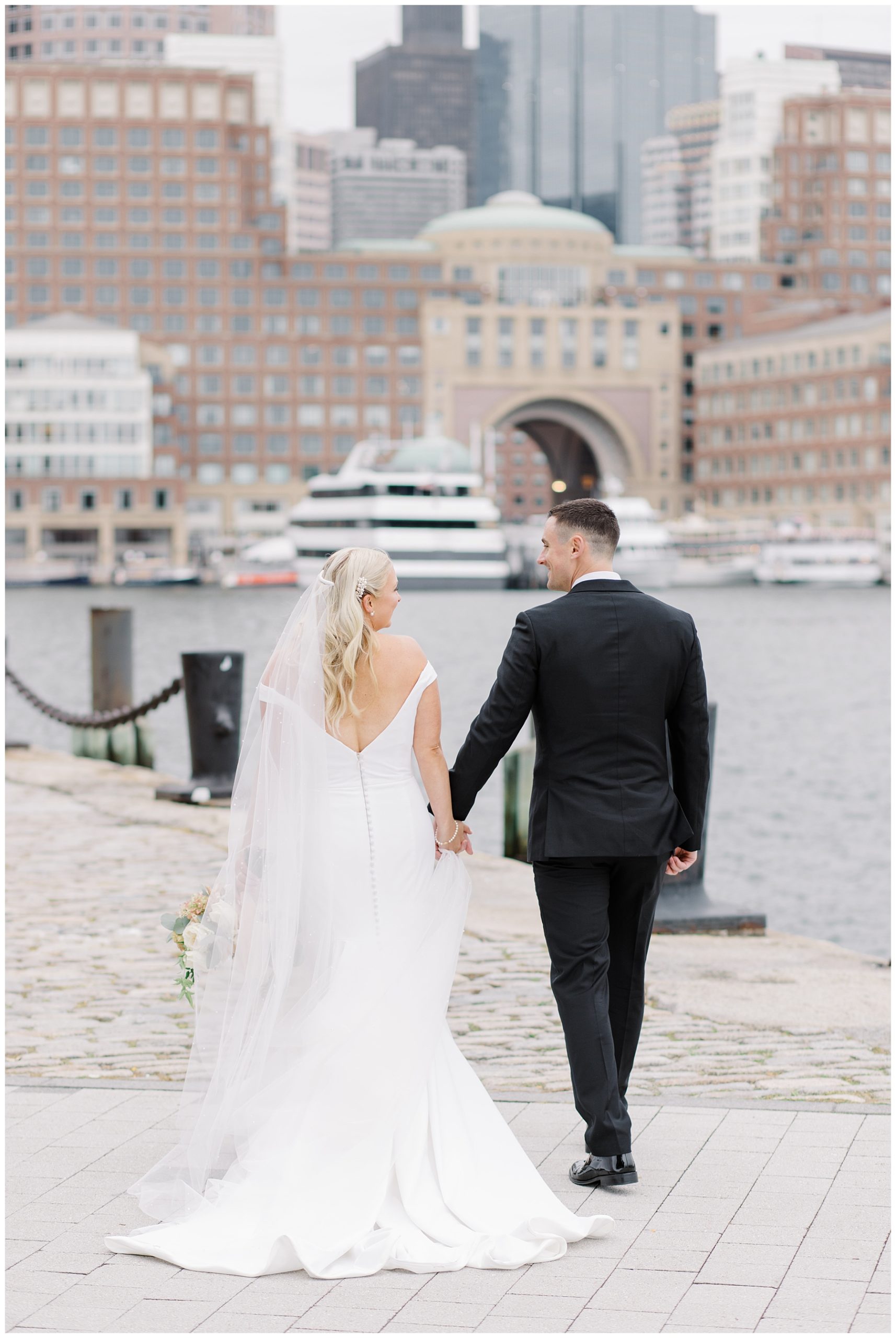 couple walk along Boston Pier holding hands