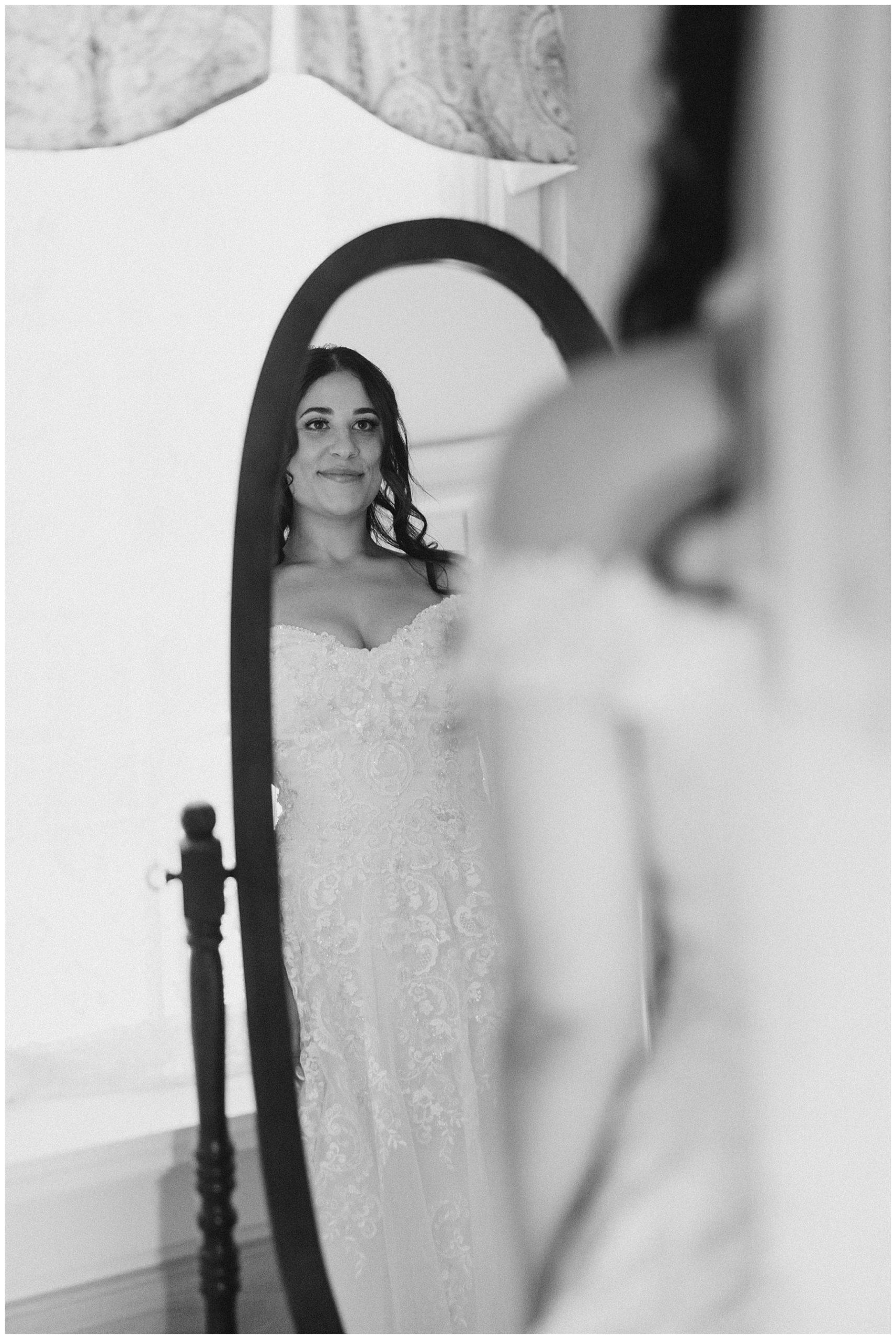 Bride looks in mirror after putting on wedding gown