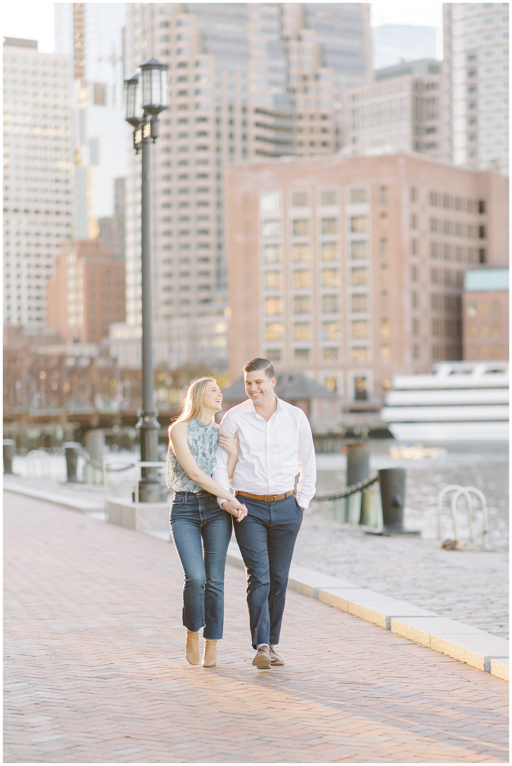 newly engaged couple walk together holding hands at Boston Harbor