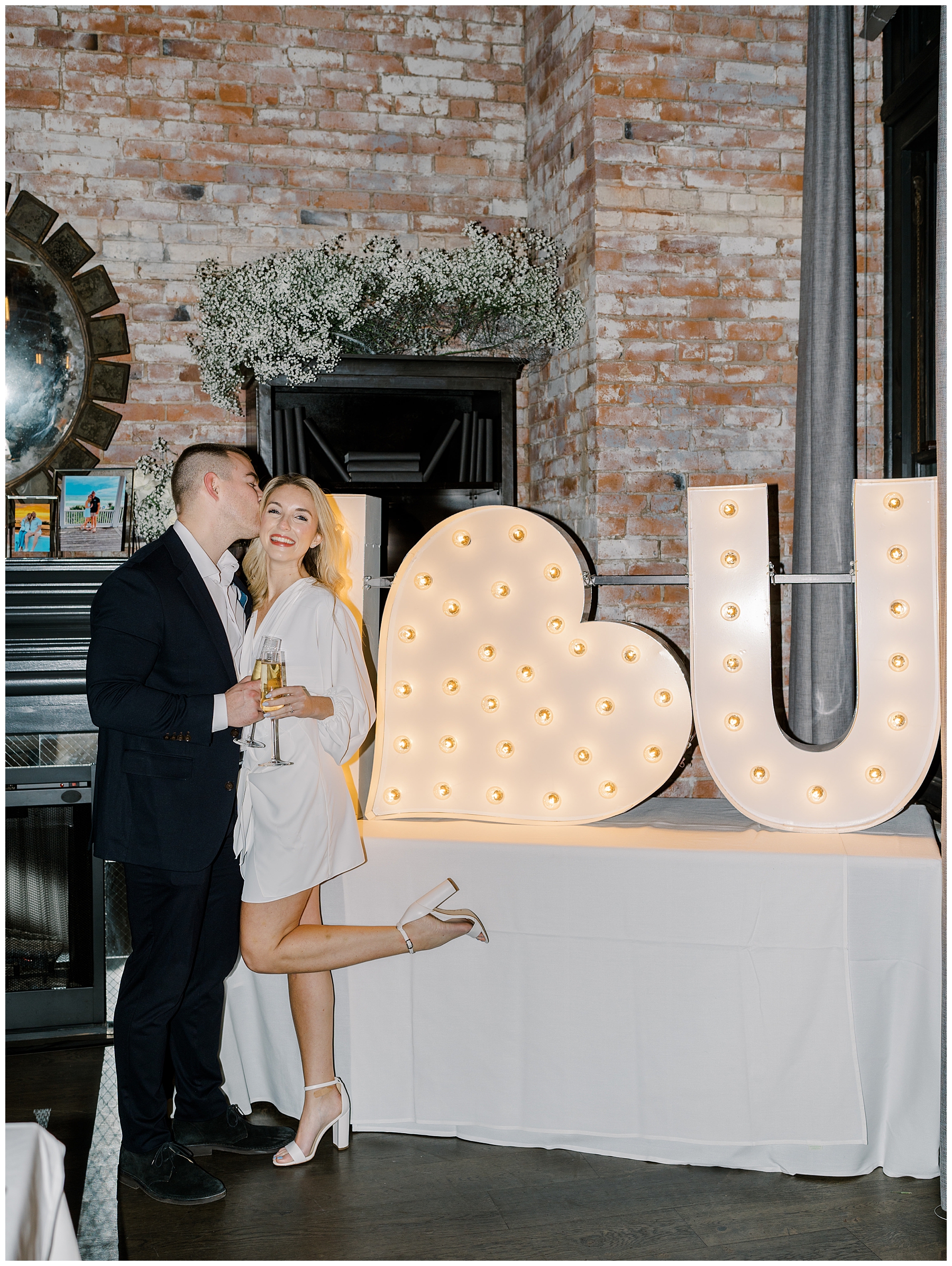nelwy engaged couple stand by large light up I Love you sign 