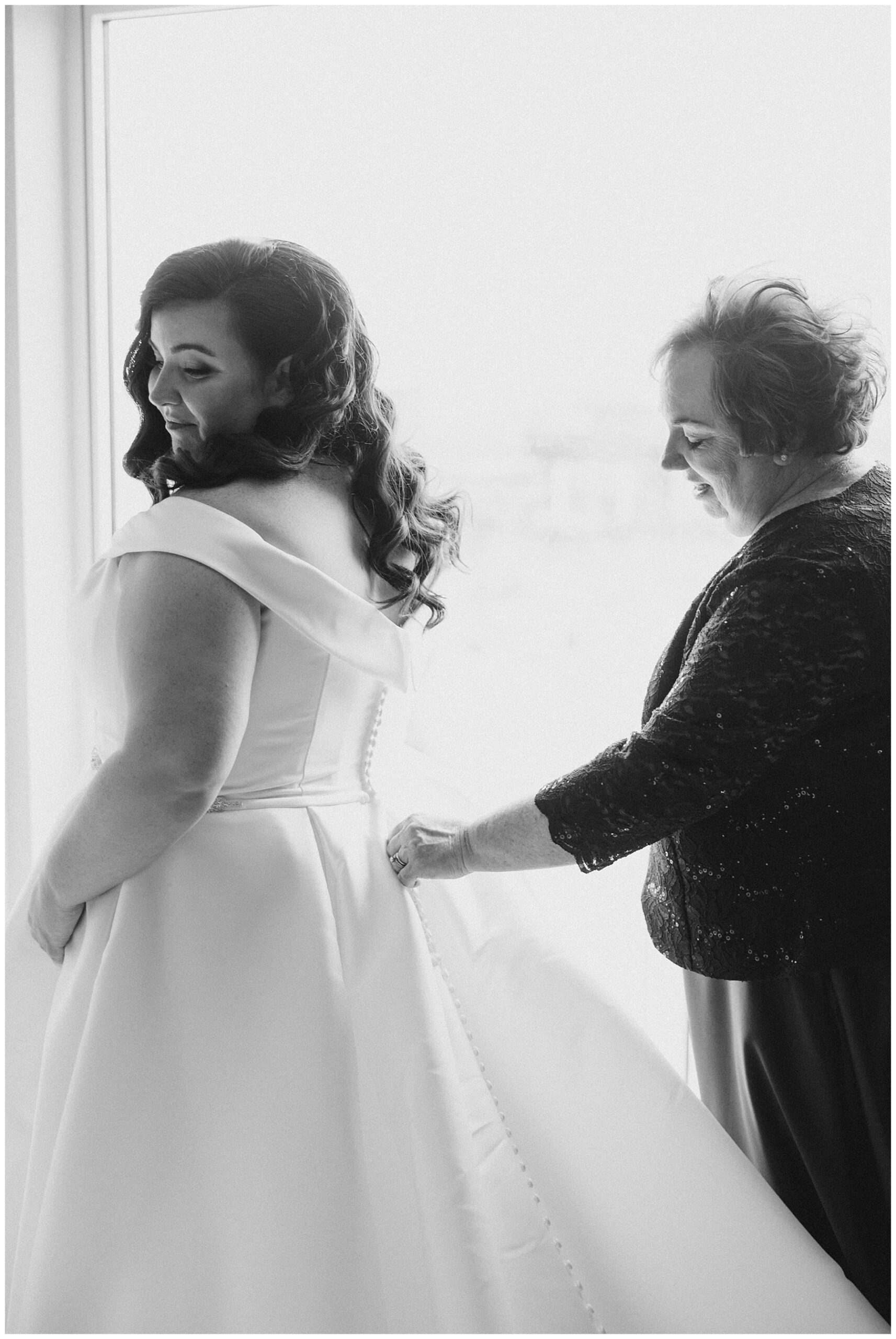 mother of the bride helping daughter into wedding dress