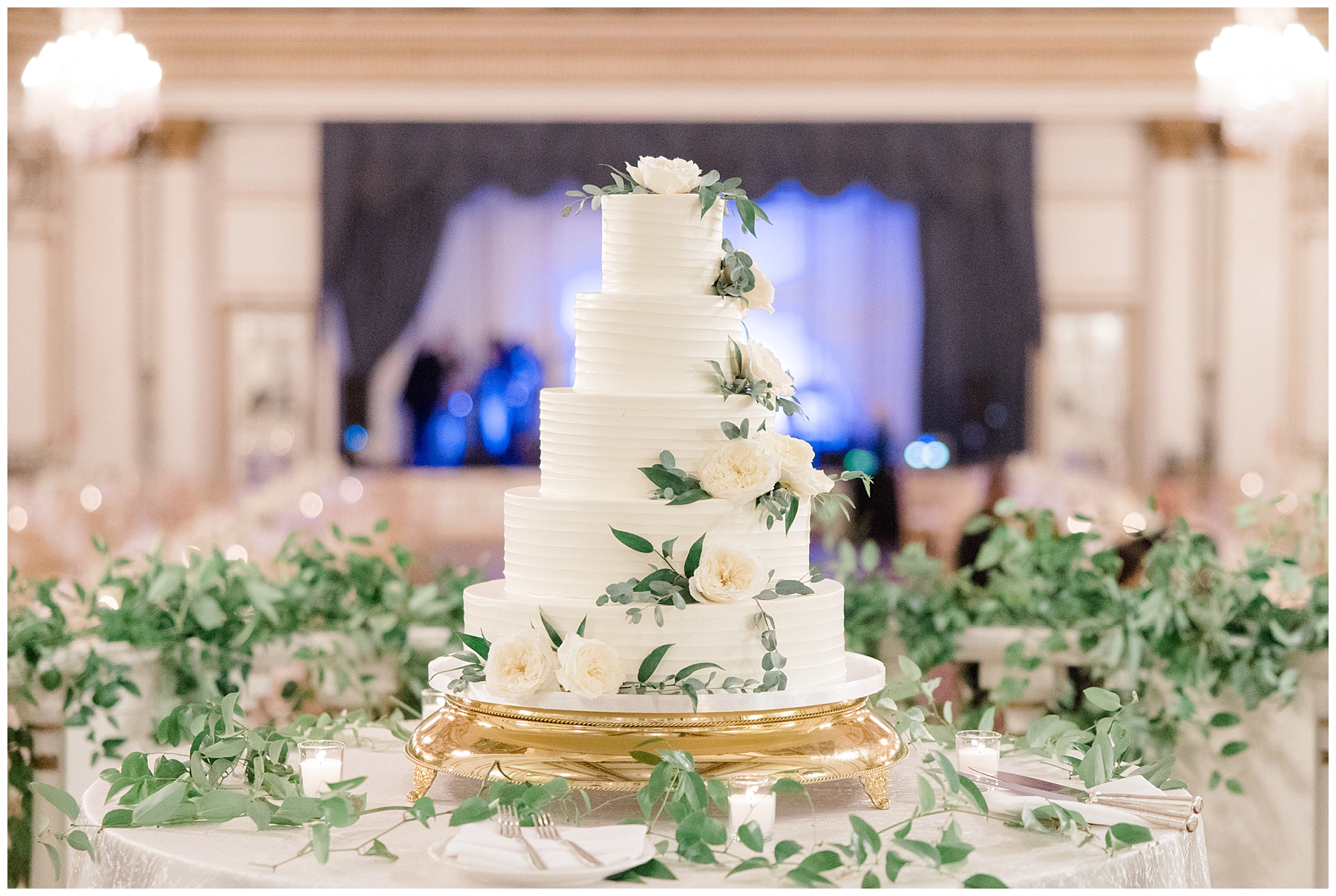 5 tired classic white wedding cake decorated with white flowers and surrounded by greenery
