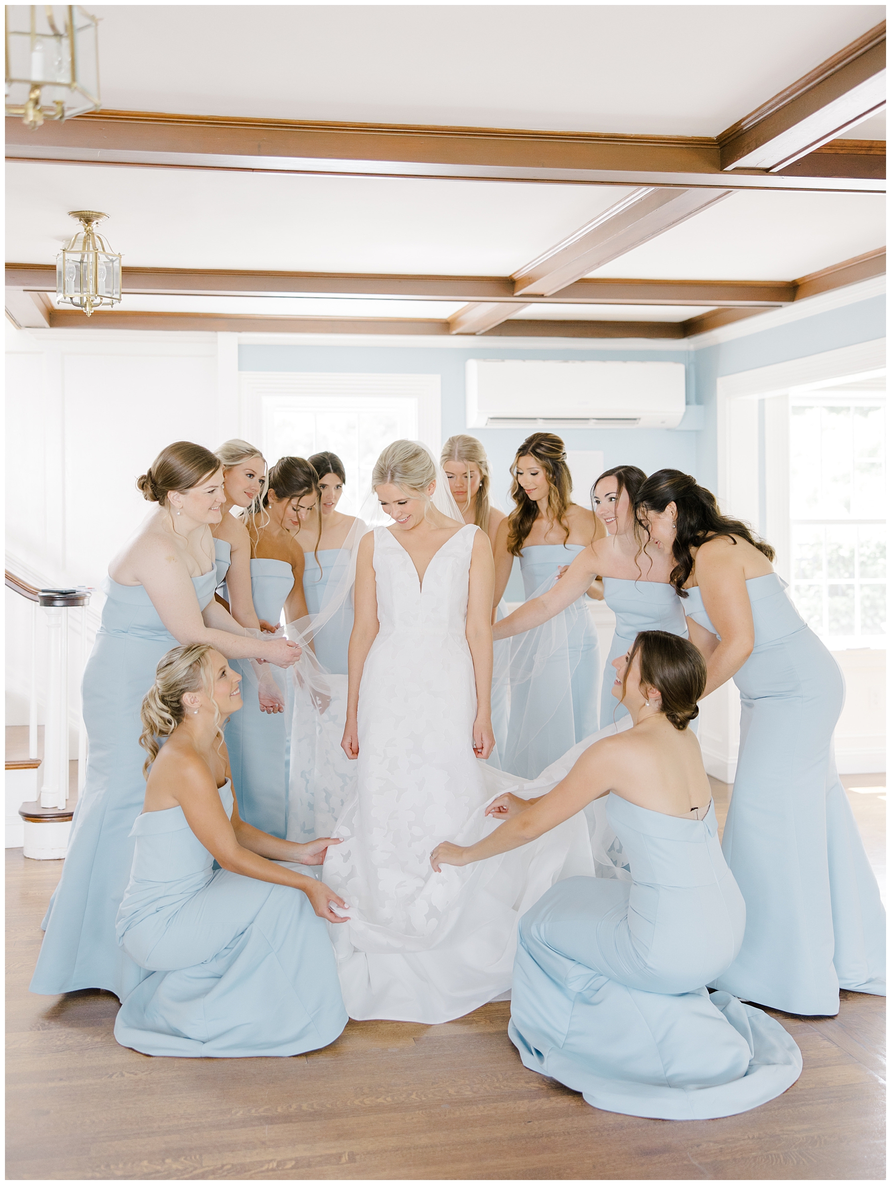 bridesmaids in dusty blue dresses help bride with dress
