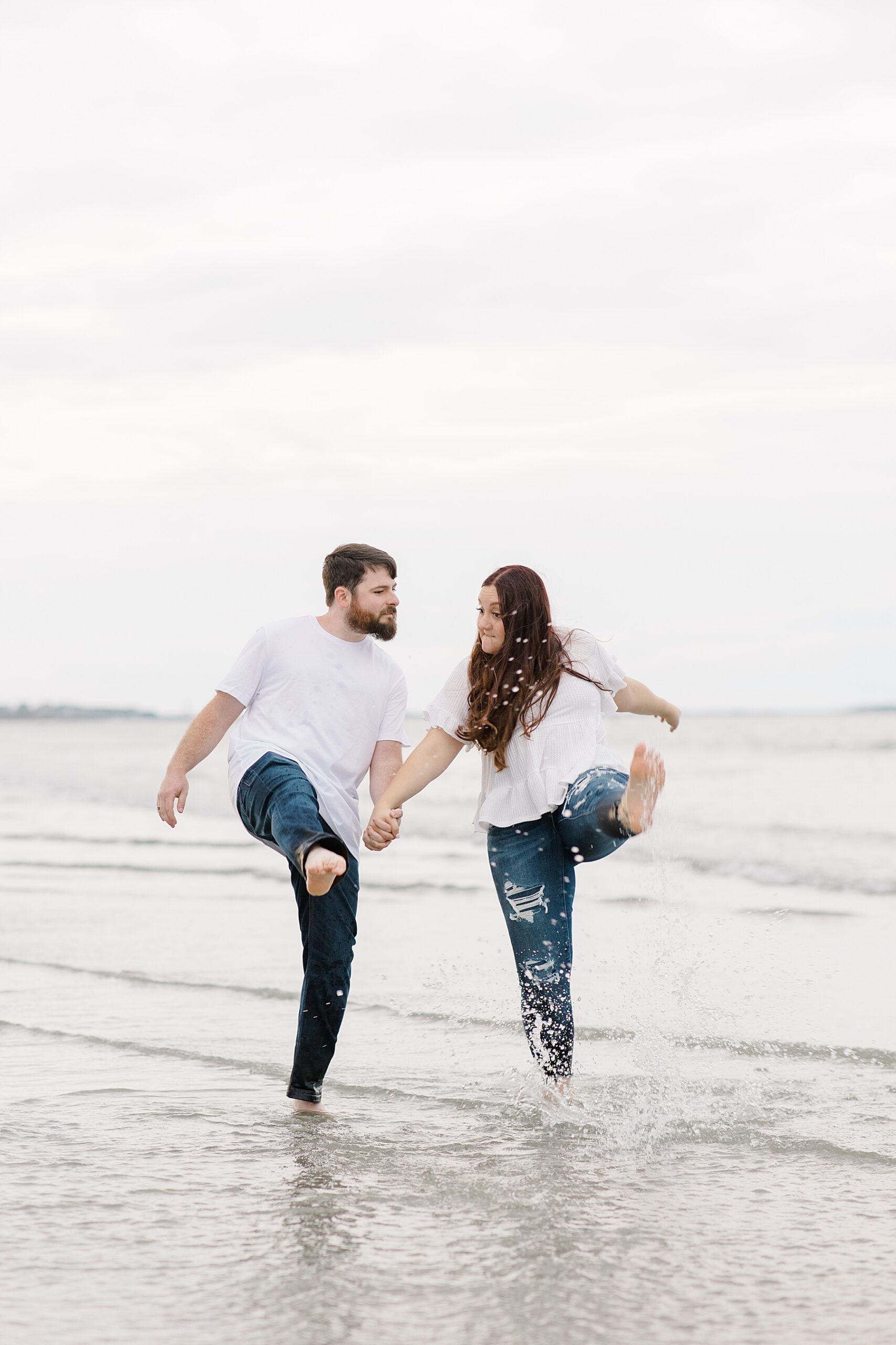 engaged couple kick up the water during Romantic Nantasket Beach Engagement