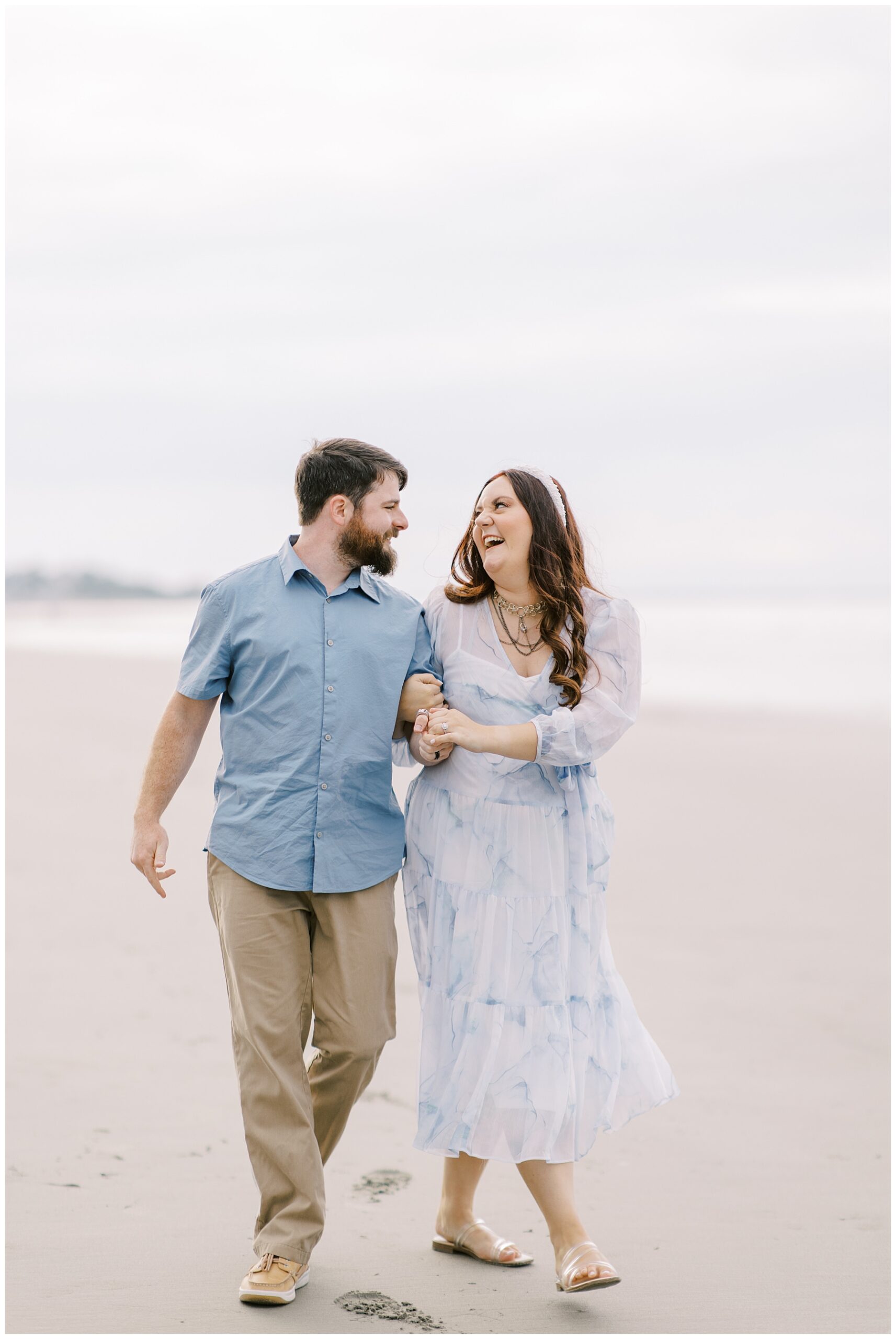 engaged couple laugh together as they walk the beach