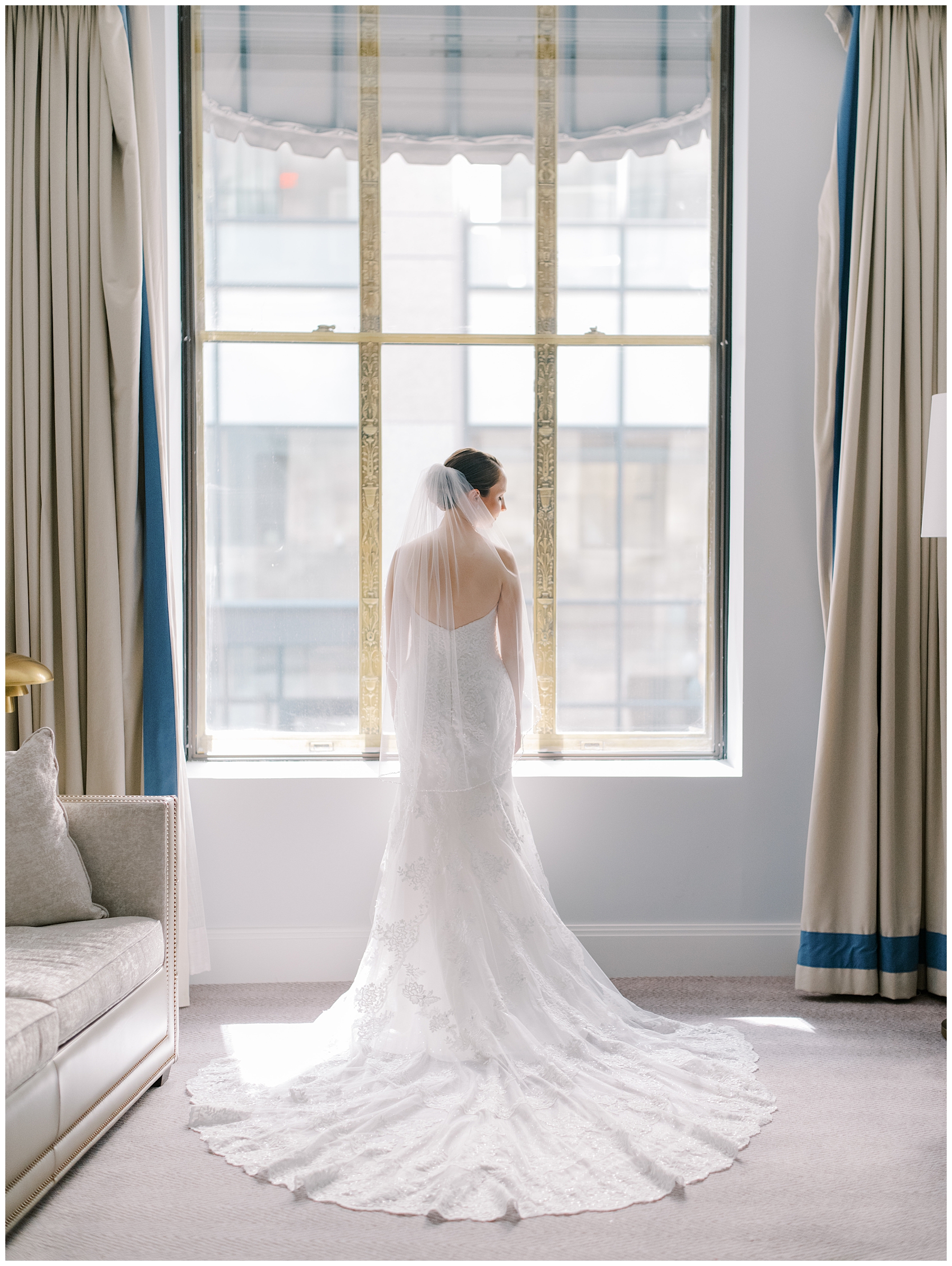 bride looks out window showing off back of bride's wedding dress