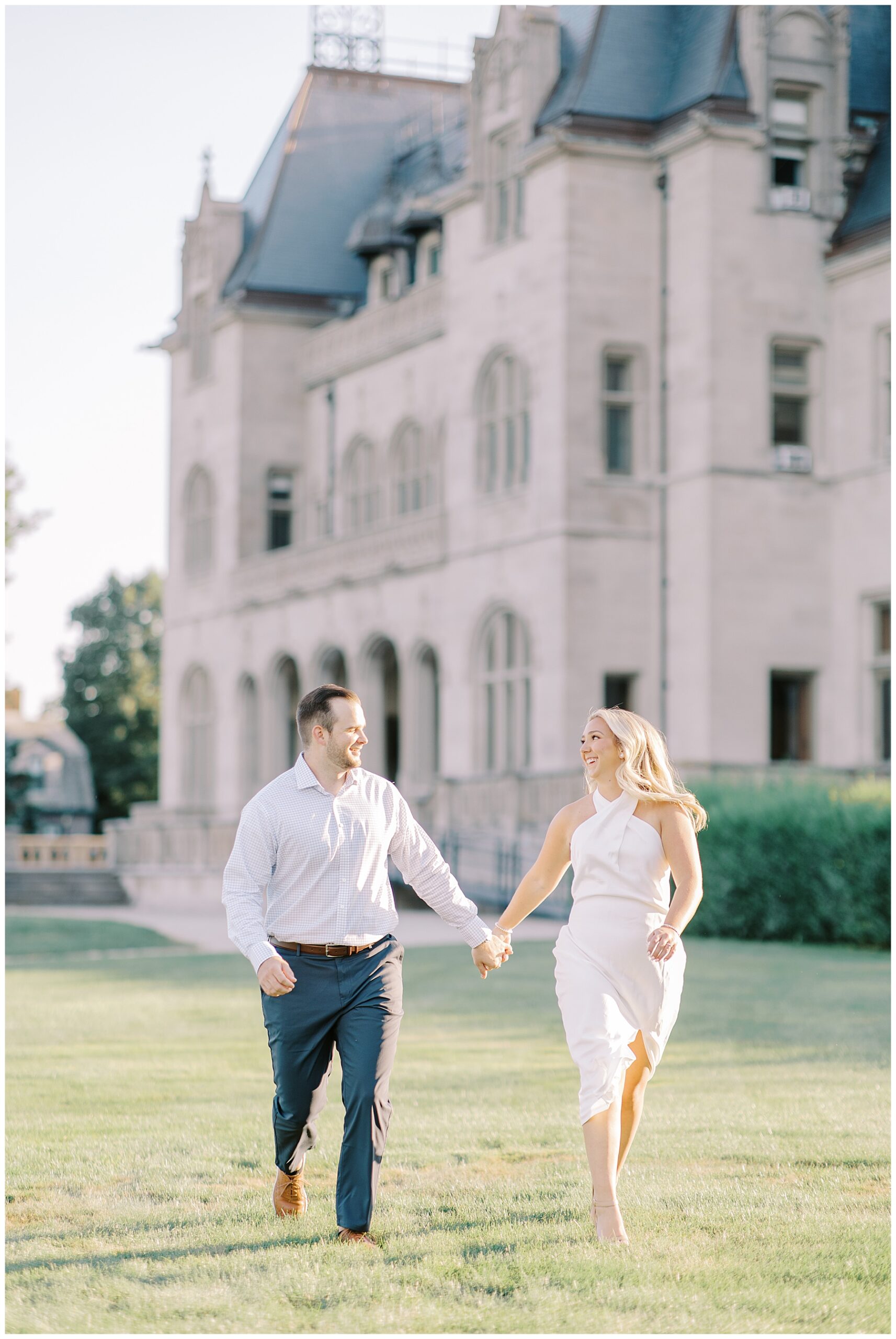 couple hold hands as they run across grounds of Ochre Court  during Engagement session