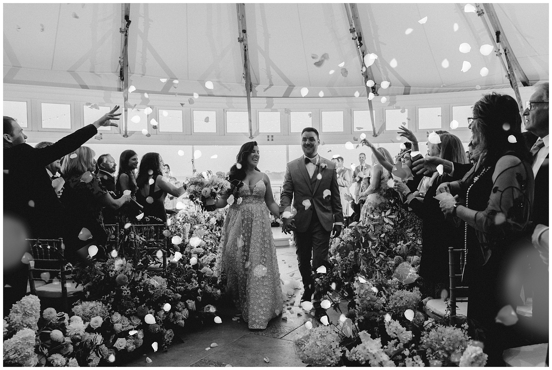 guests throw flower petals at newlyweds as they exit wedding ceremony