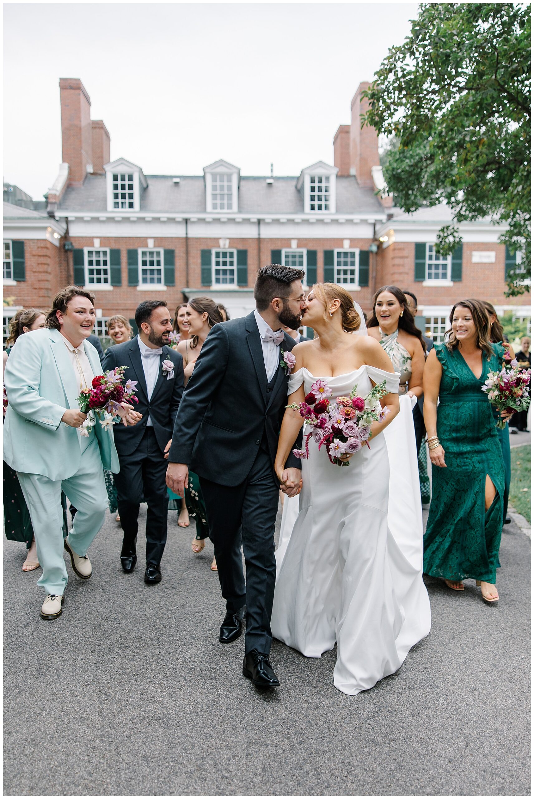 newlyweds kiss as wedding party walk behind the couple
