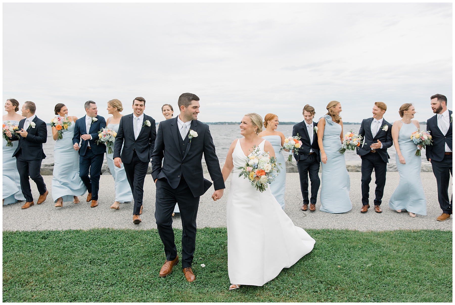 bride and groom walk and hold hands with wedding party behind them