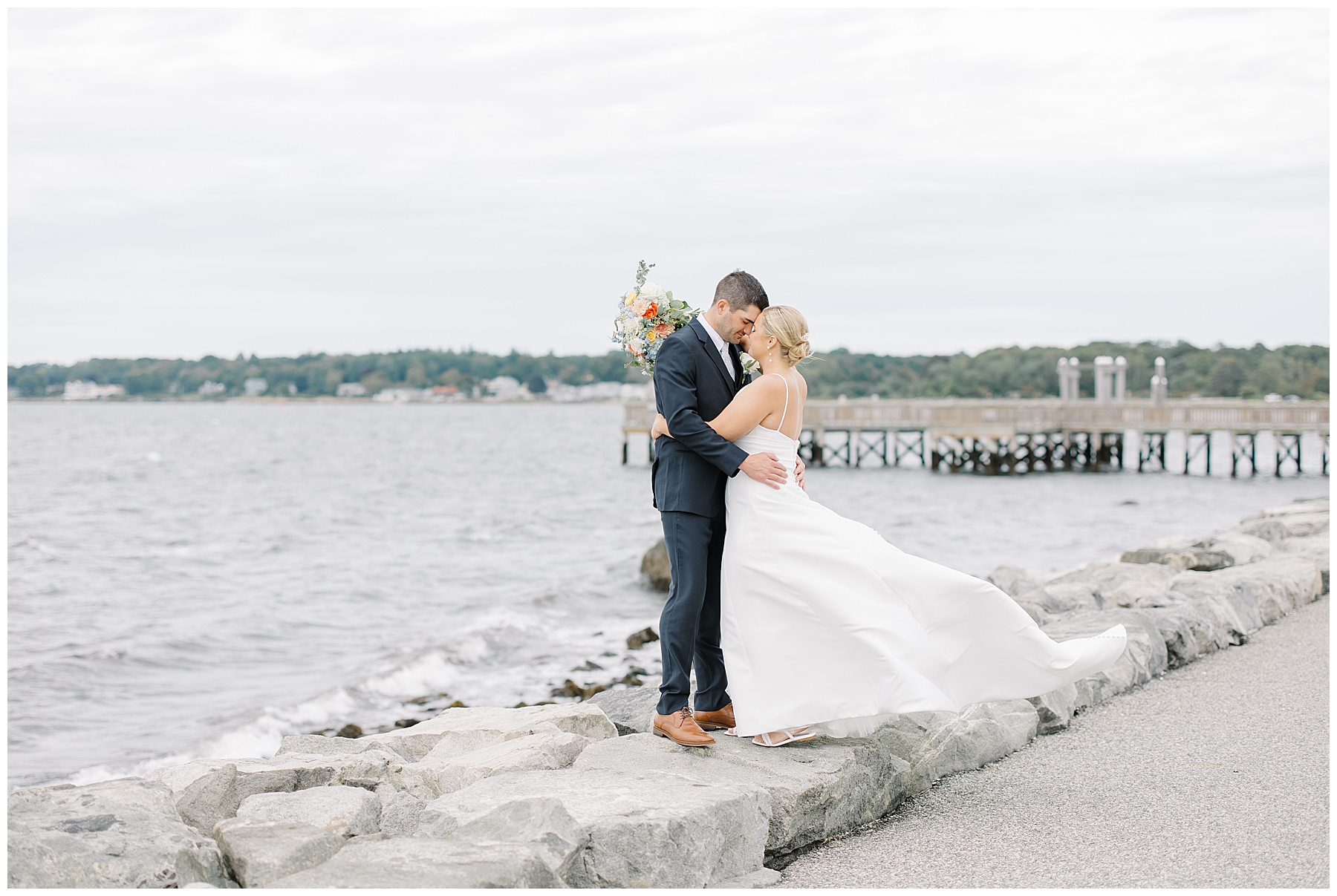 bride and groom stand on rocks by the water