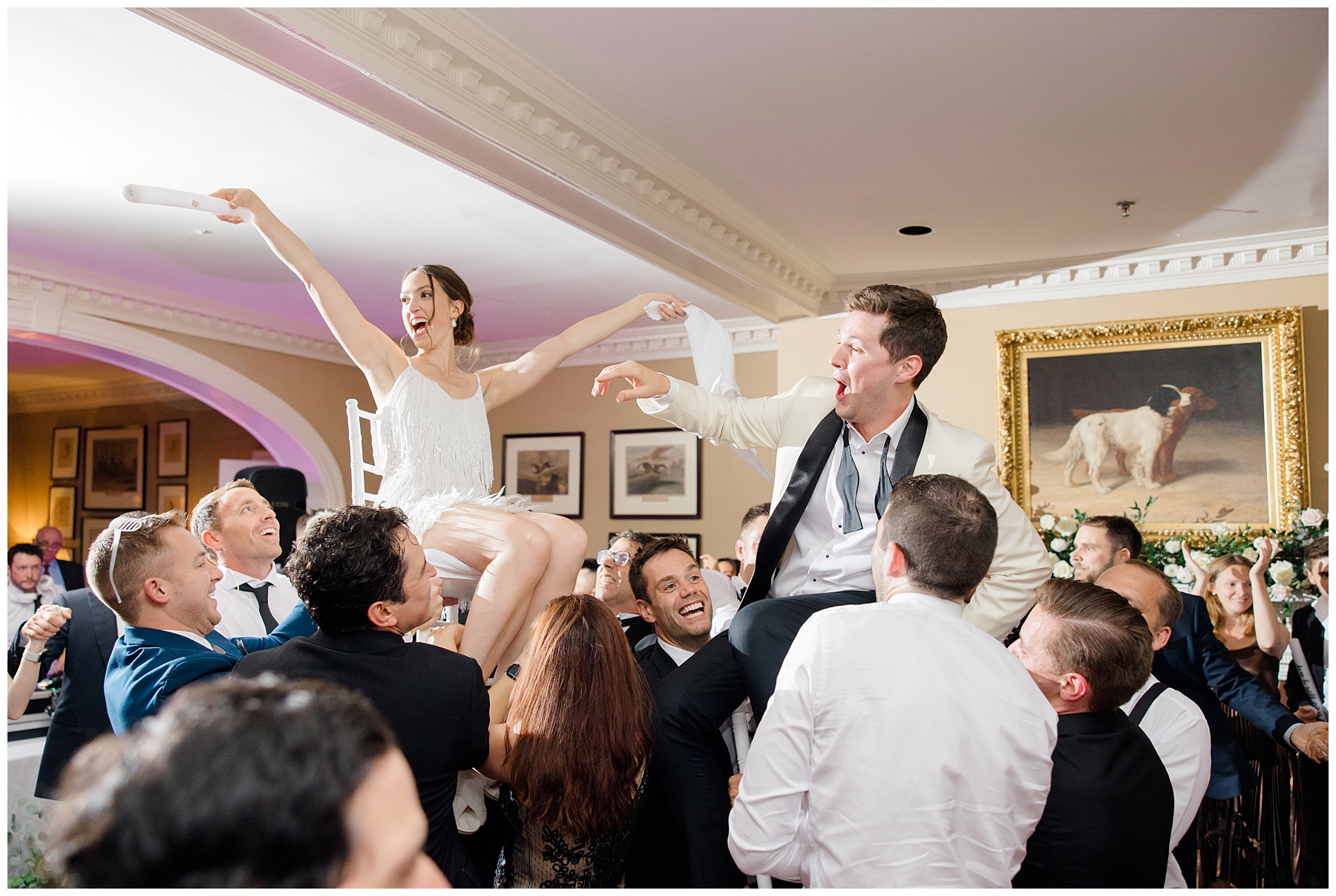 wedding guests lift bride and groom up in chairs