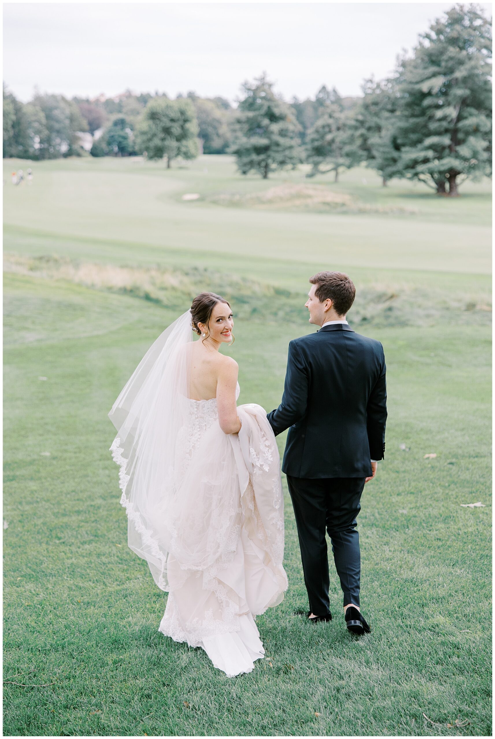 bride and groom hold hands as they walk across the golf course at  The Country Club in Brookline, MA