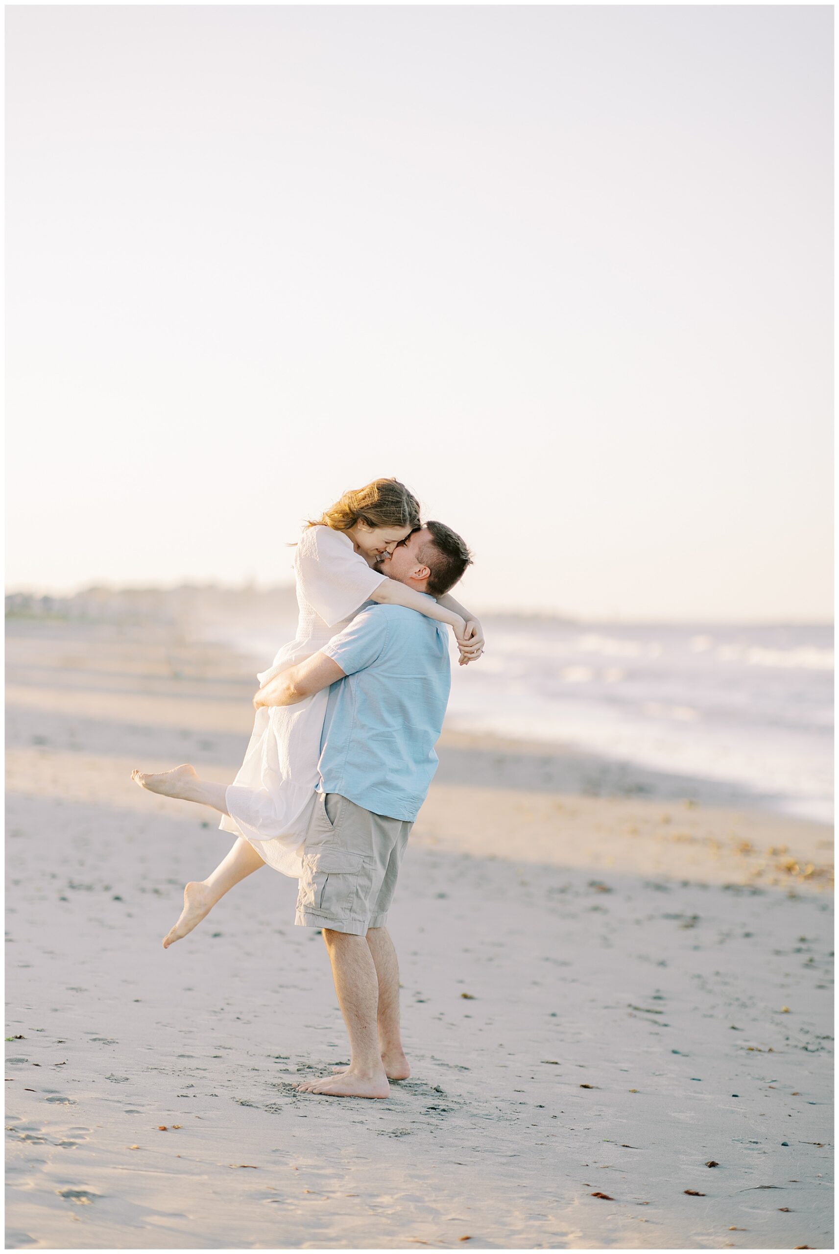 romantic engagement portraits of man lifting fiancé on Nantasket Beach