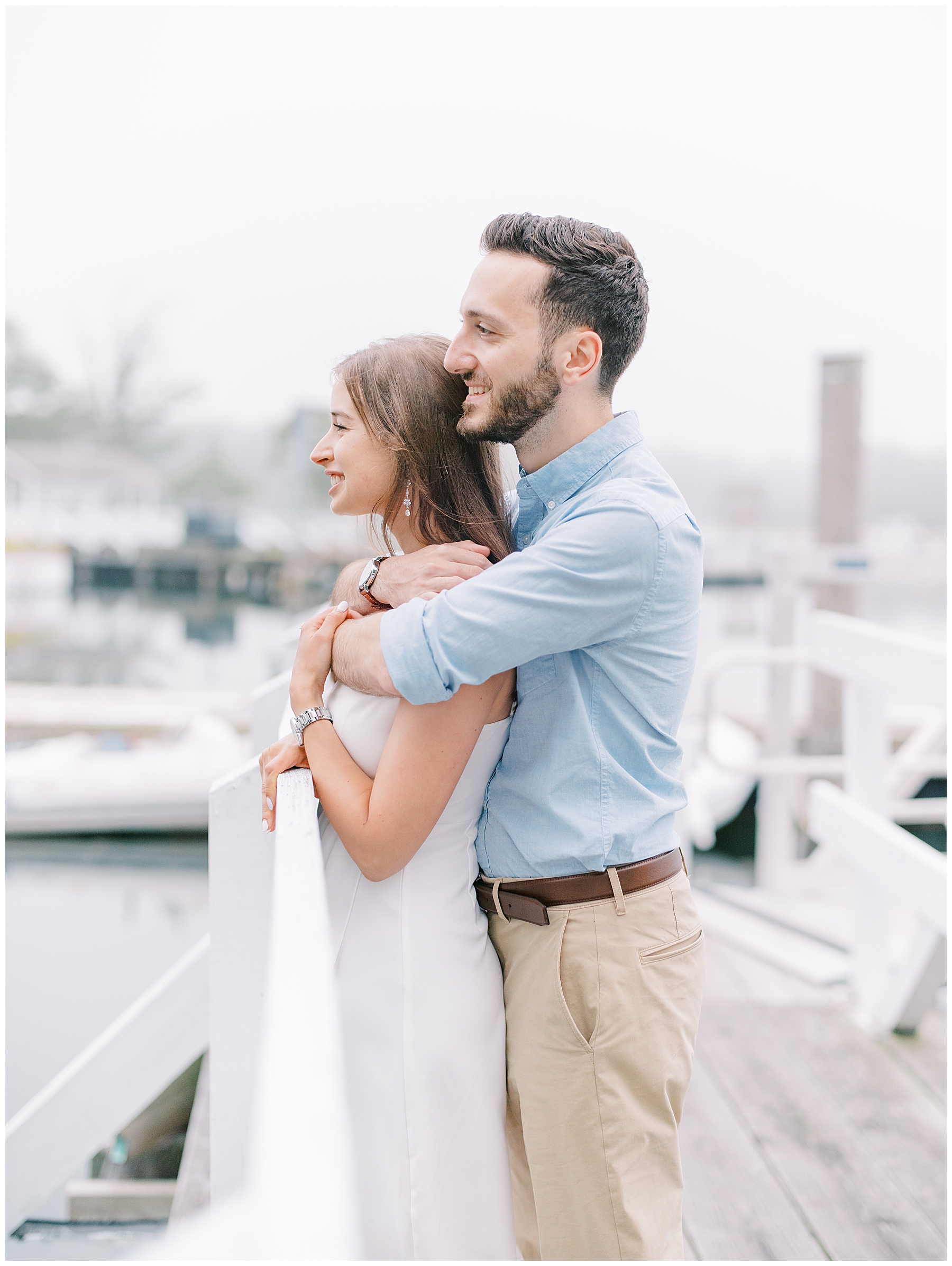 couple stand on dock at beach during Boston beach engagement