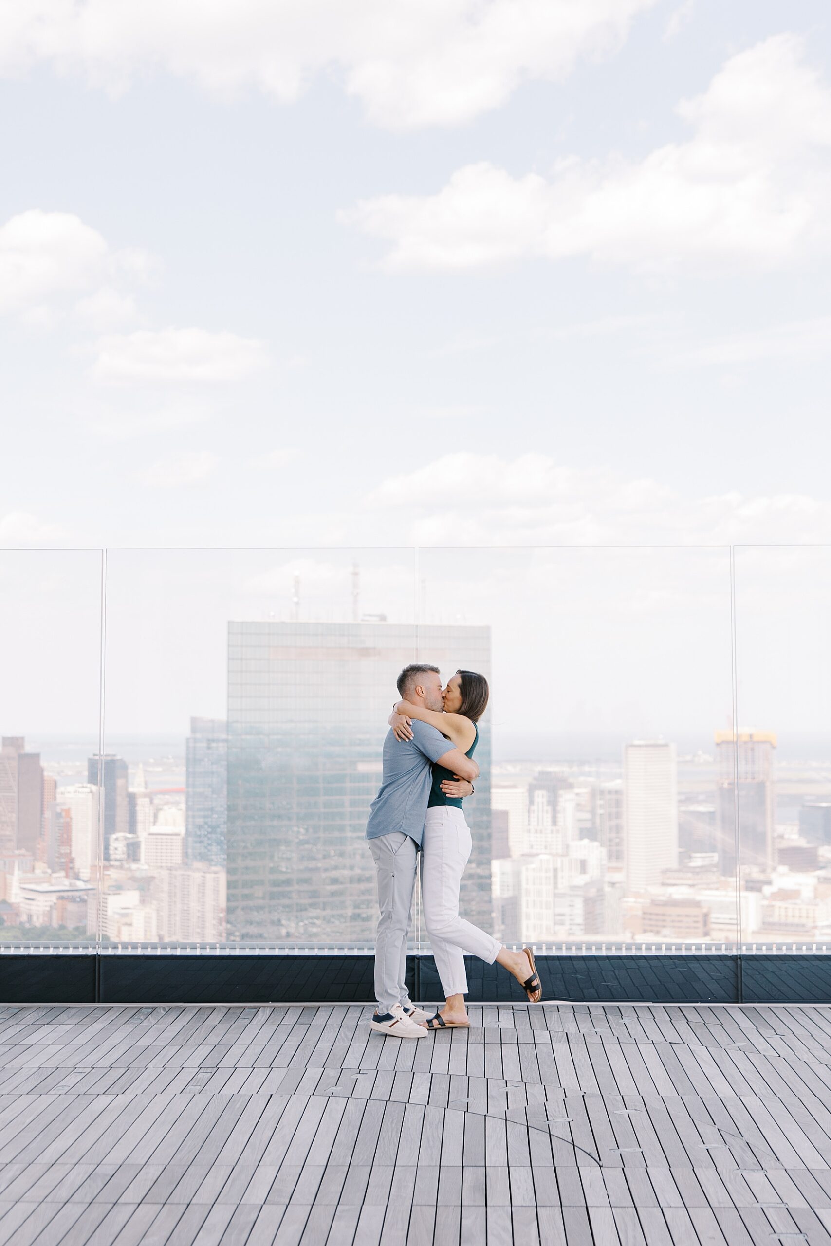 newly engaged couple kiss with Boston skyline in the distance