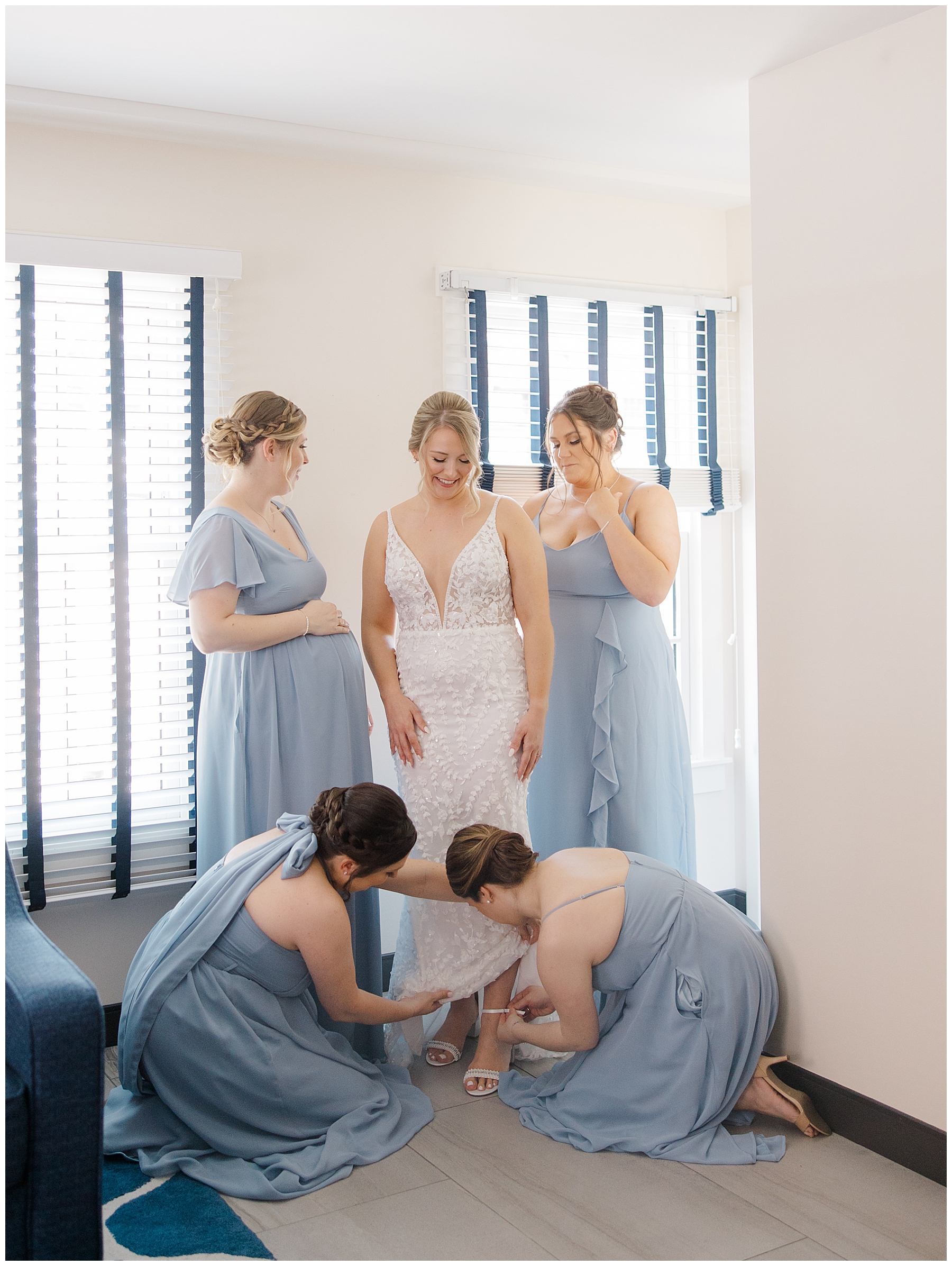 bridesmaids in blue dresses help bride with shoes