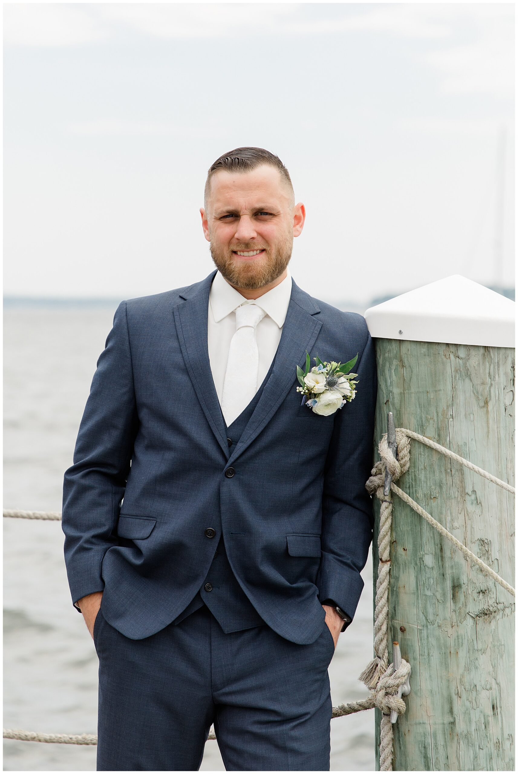 groom leans by wooden post on dock before first look