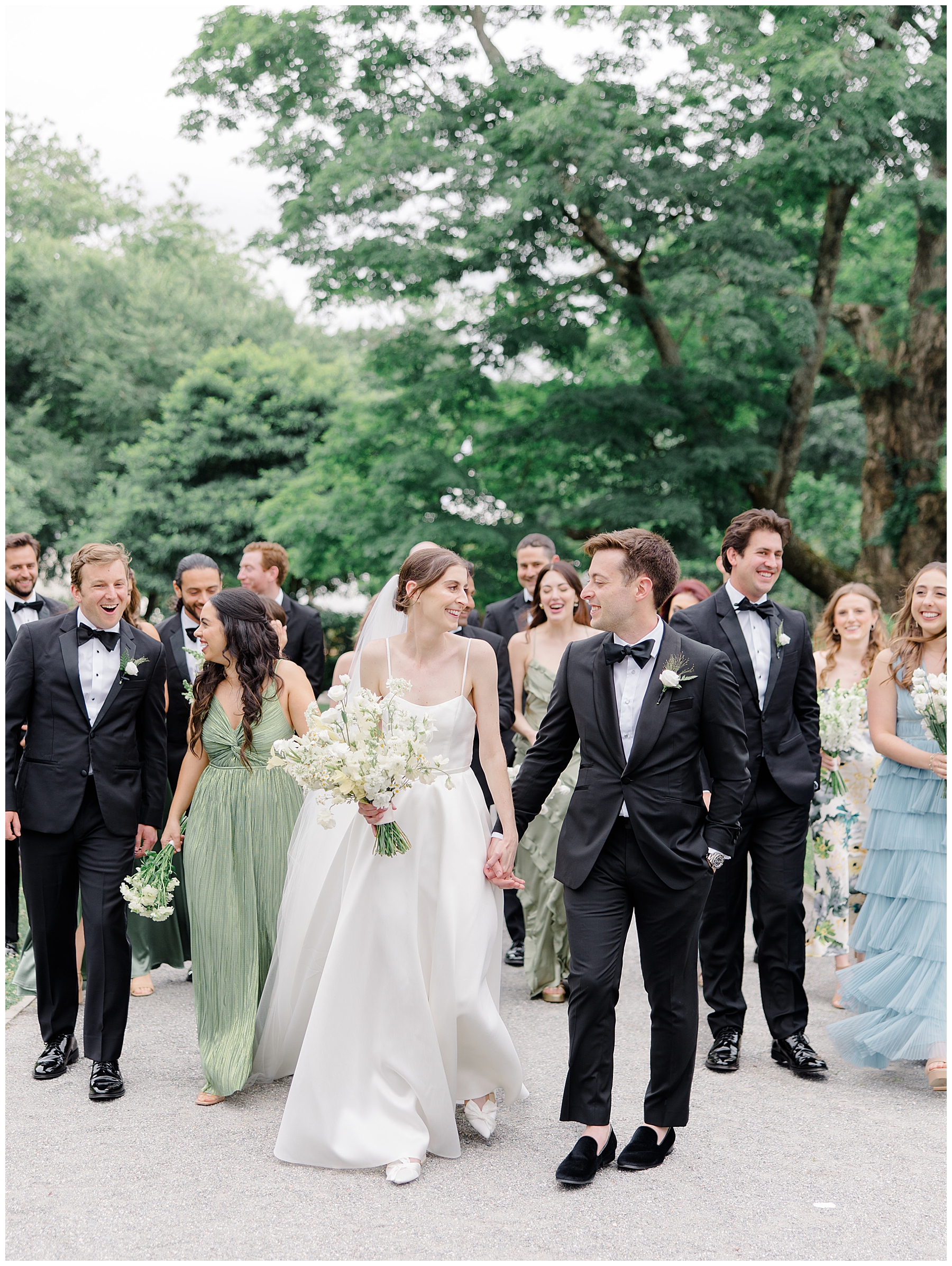 bride and groom walk together with bridal party behind them 