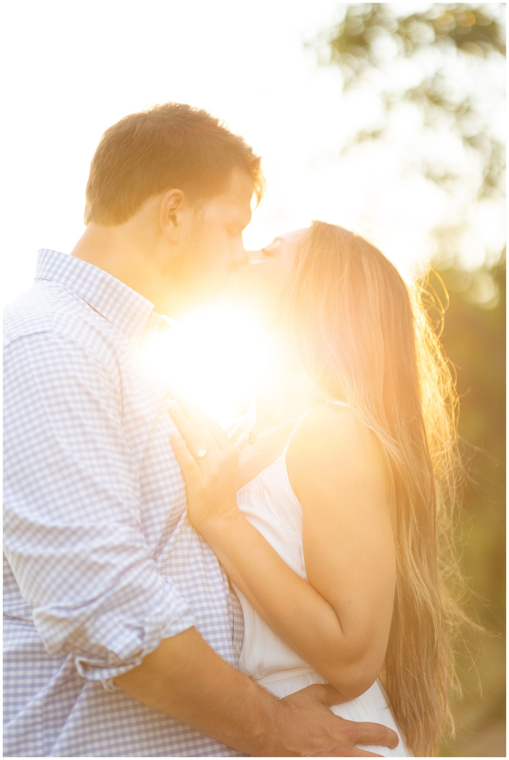 couple kiss as the sun shines behind them