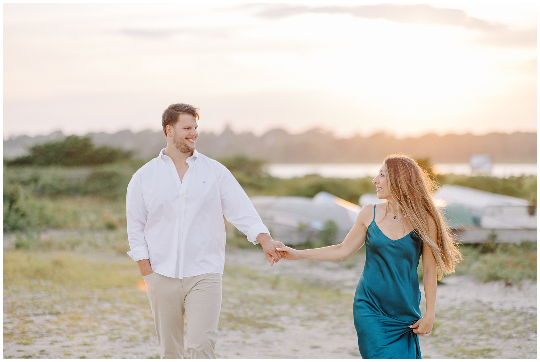 couple hold hands as they walk along the beach at sunset