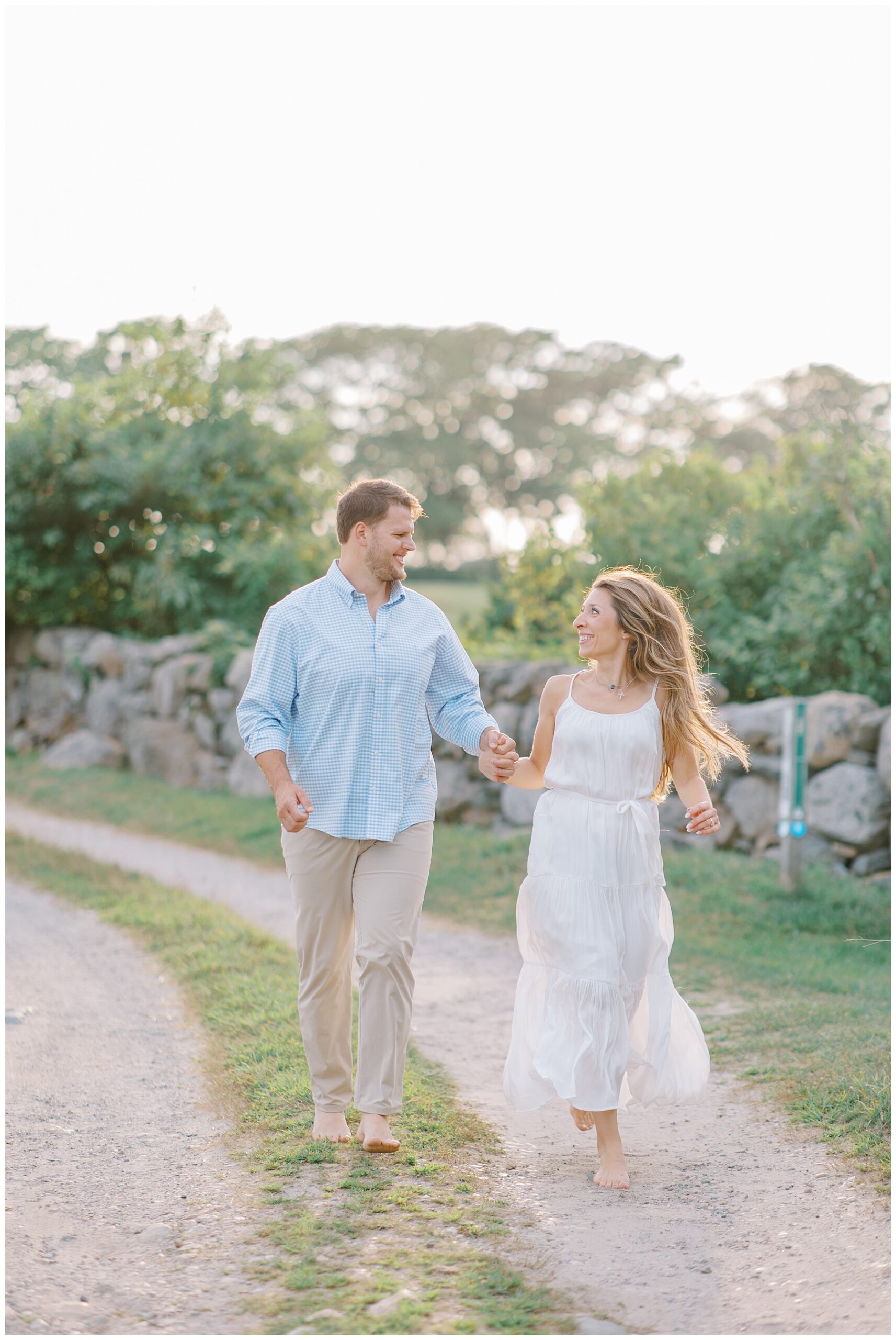 engaged couple hold hands as they walk together down path
