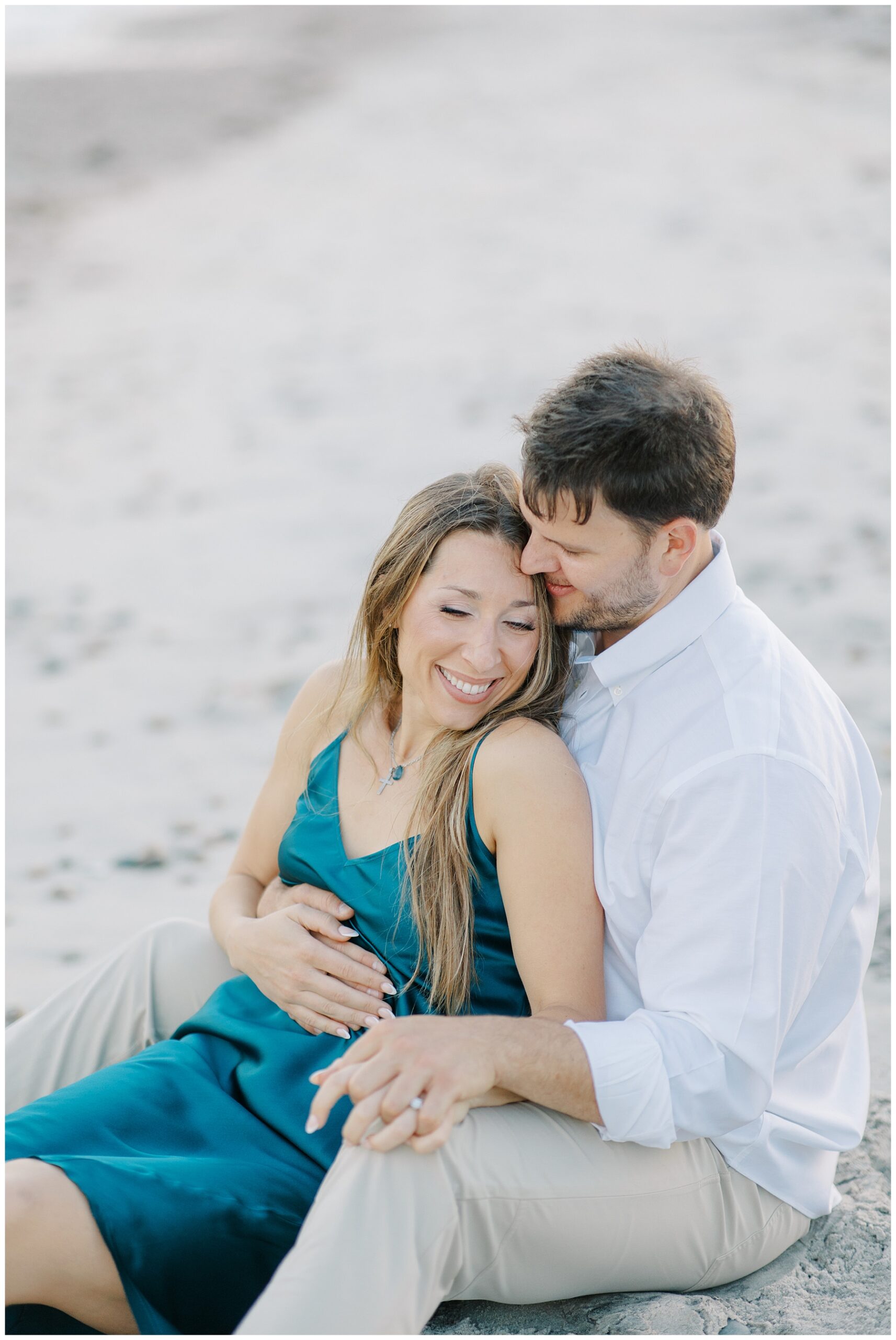candid engagement photo of couple sitting on the beach