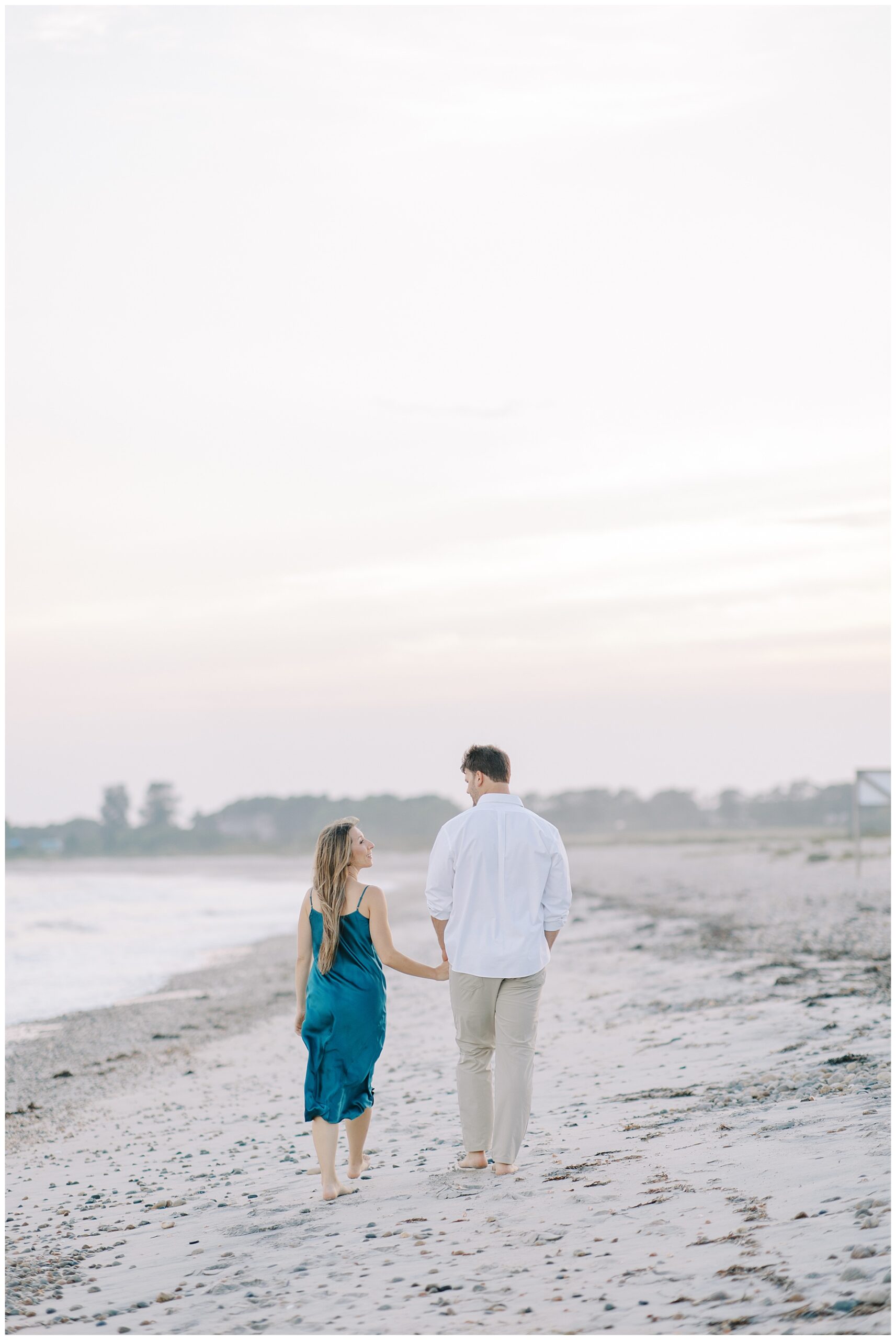 engaged couple holding hands as they walk down beach