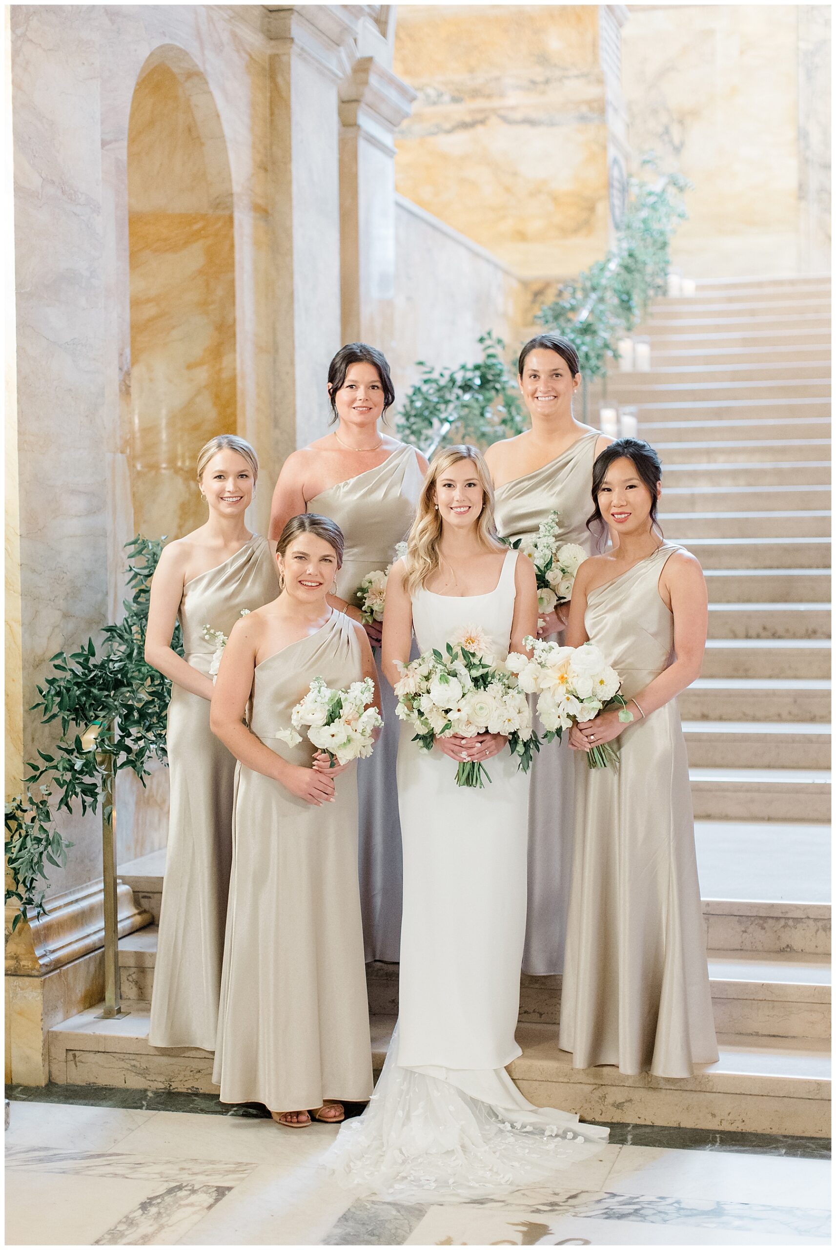 bridesmaids in champagne dresses surround bride on stiarcase